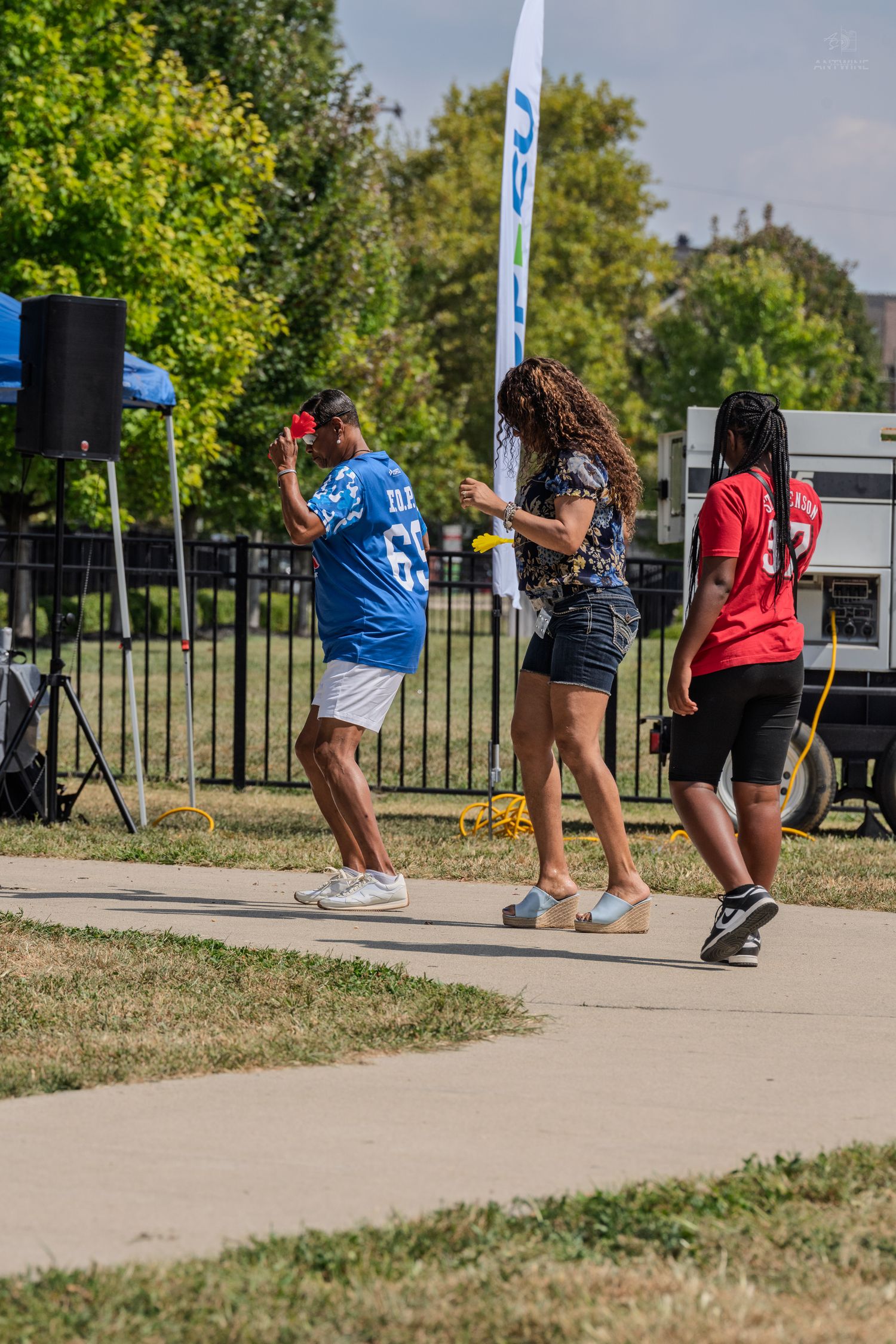People dancing and socializing outdoors at a community event near a banner on a sunny day.