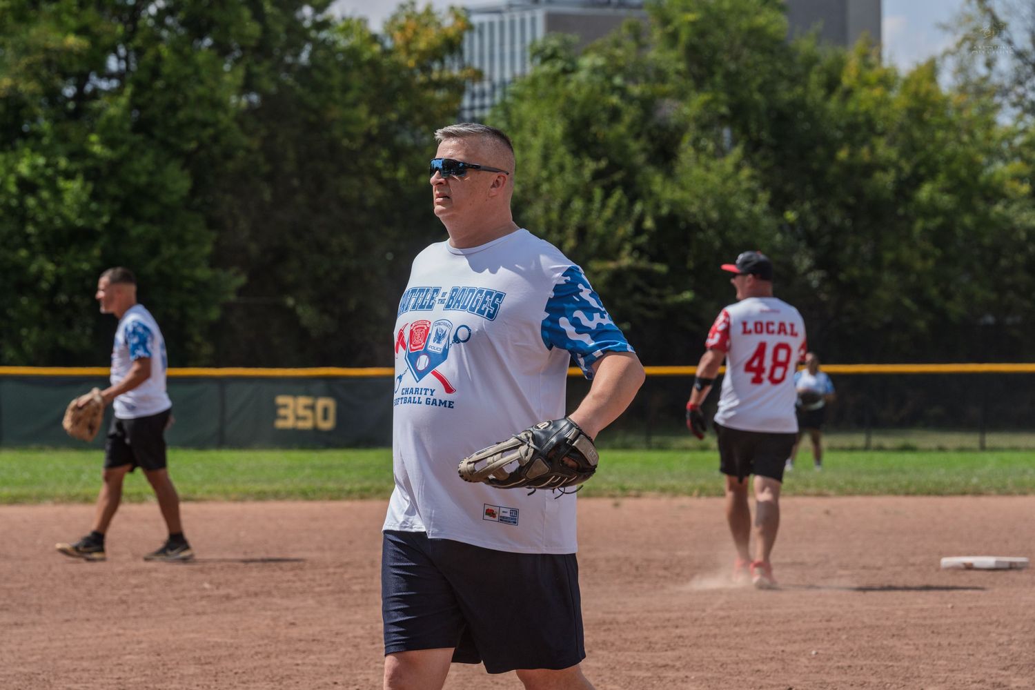 Men playing recreational softball on a sunny day wearing team jerseys with baseball gloves.