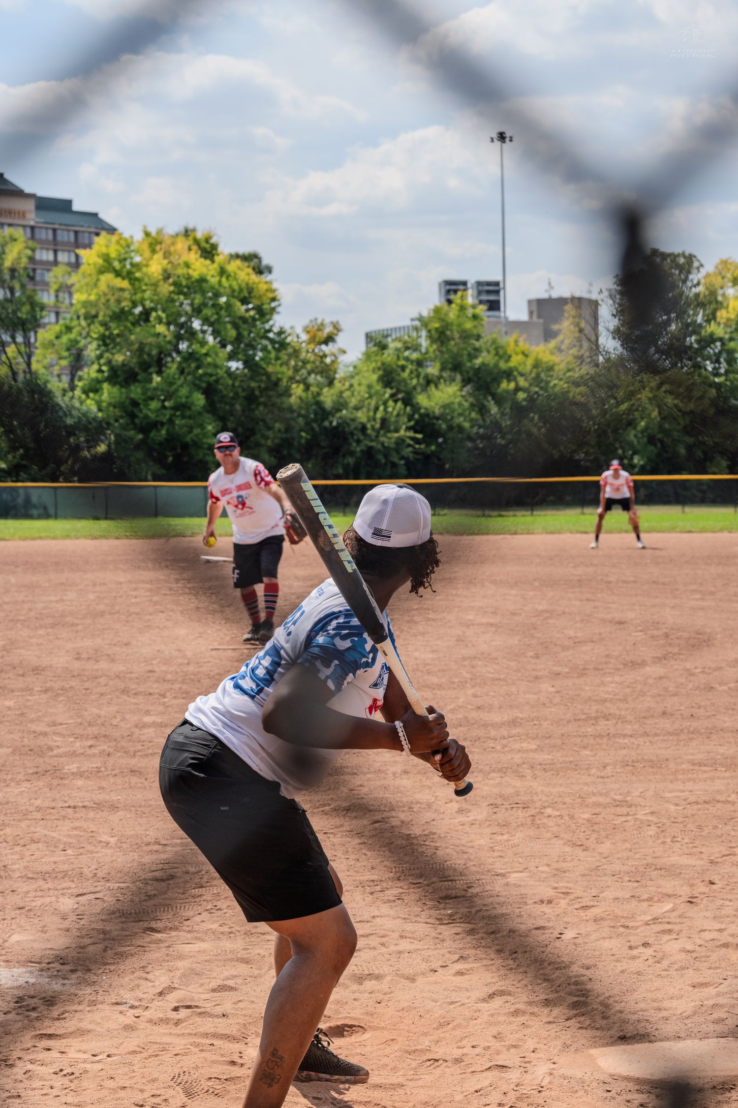 A softball player in a white jersey and black shorts prepares to bat during an outdoor game.