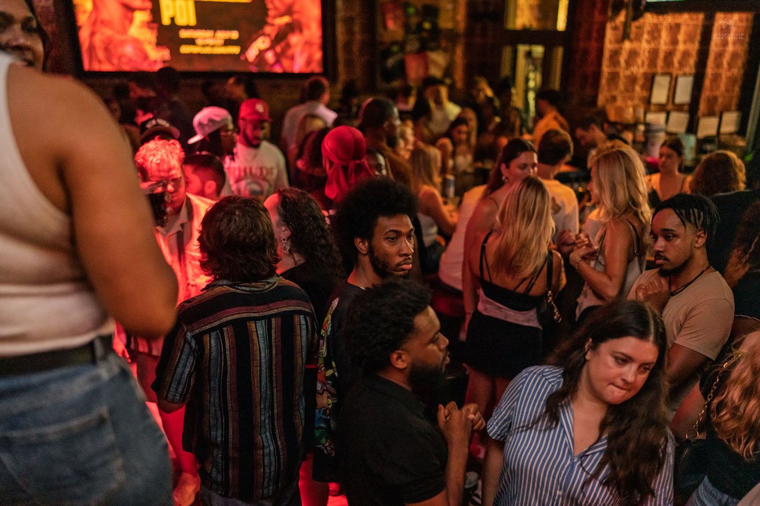 Diverse crowd of young adults socializing under warm red and ambient lighting at a nightclub.