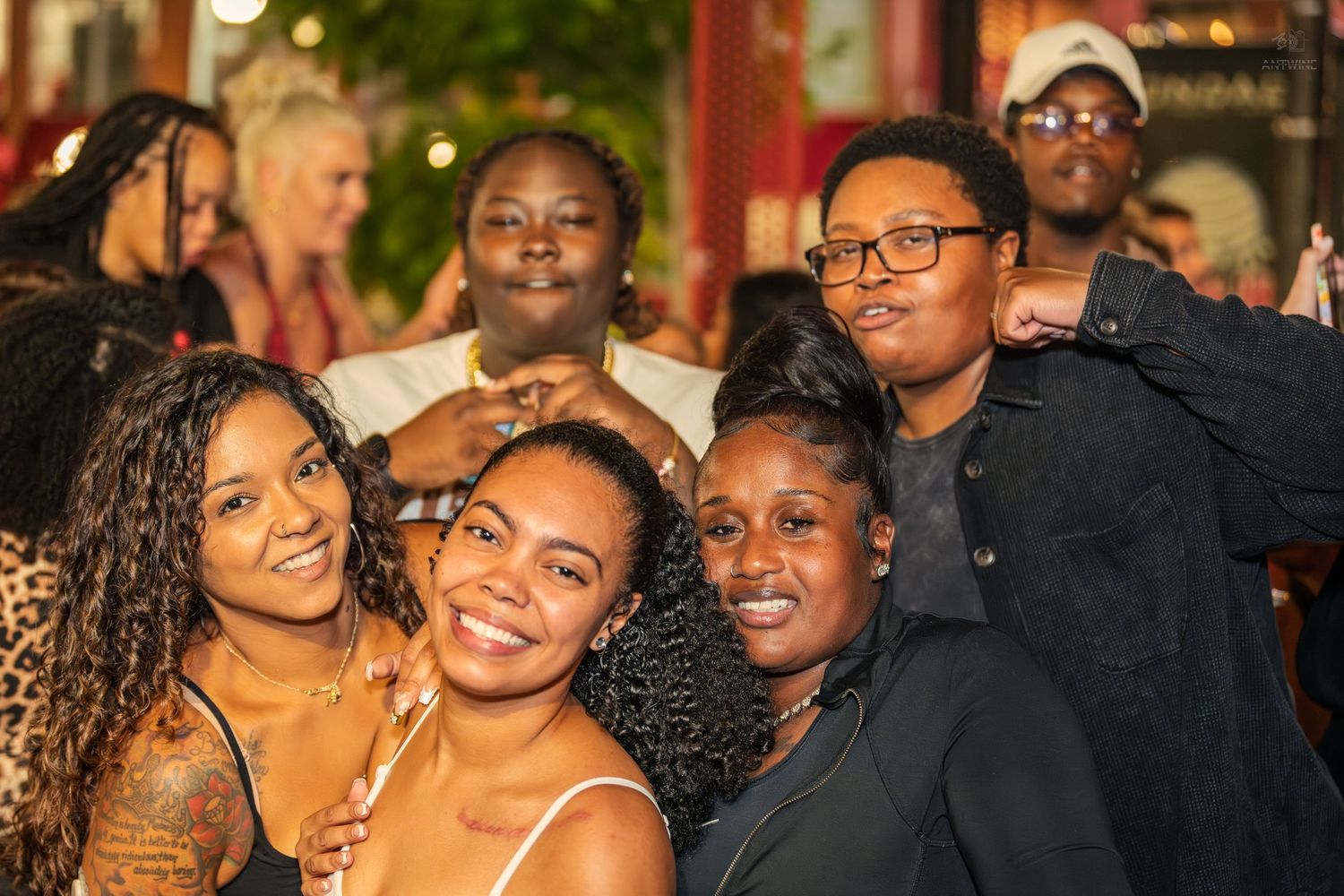 Diverse group of smiling friends posing closely together at an outdoor evening social event.