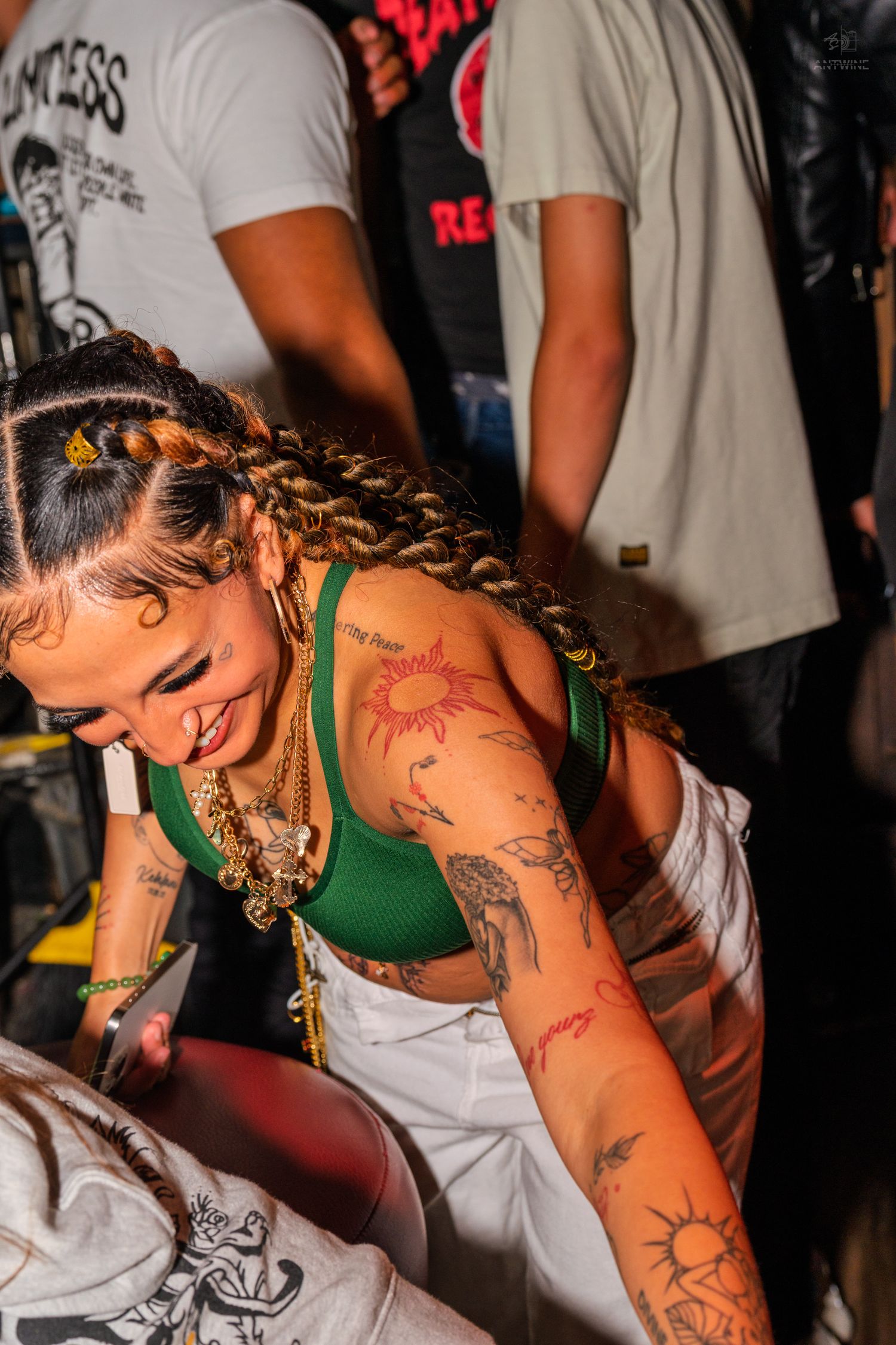 Tattooed woman with braids in a green crop top dancing at a nightclub.