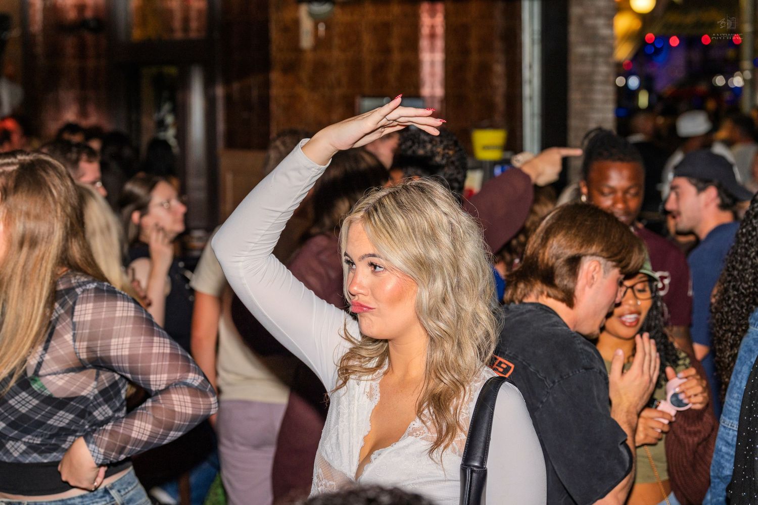 Blonde woman in white top raises her arm while dancing in a crowded outdoor nightlife venue.
