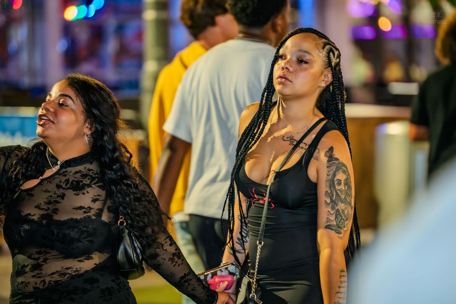 Two women in black outfits with tattoos stand together at an outdoor nighttime event.