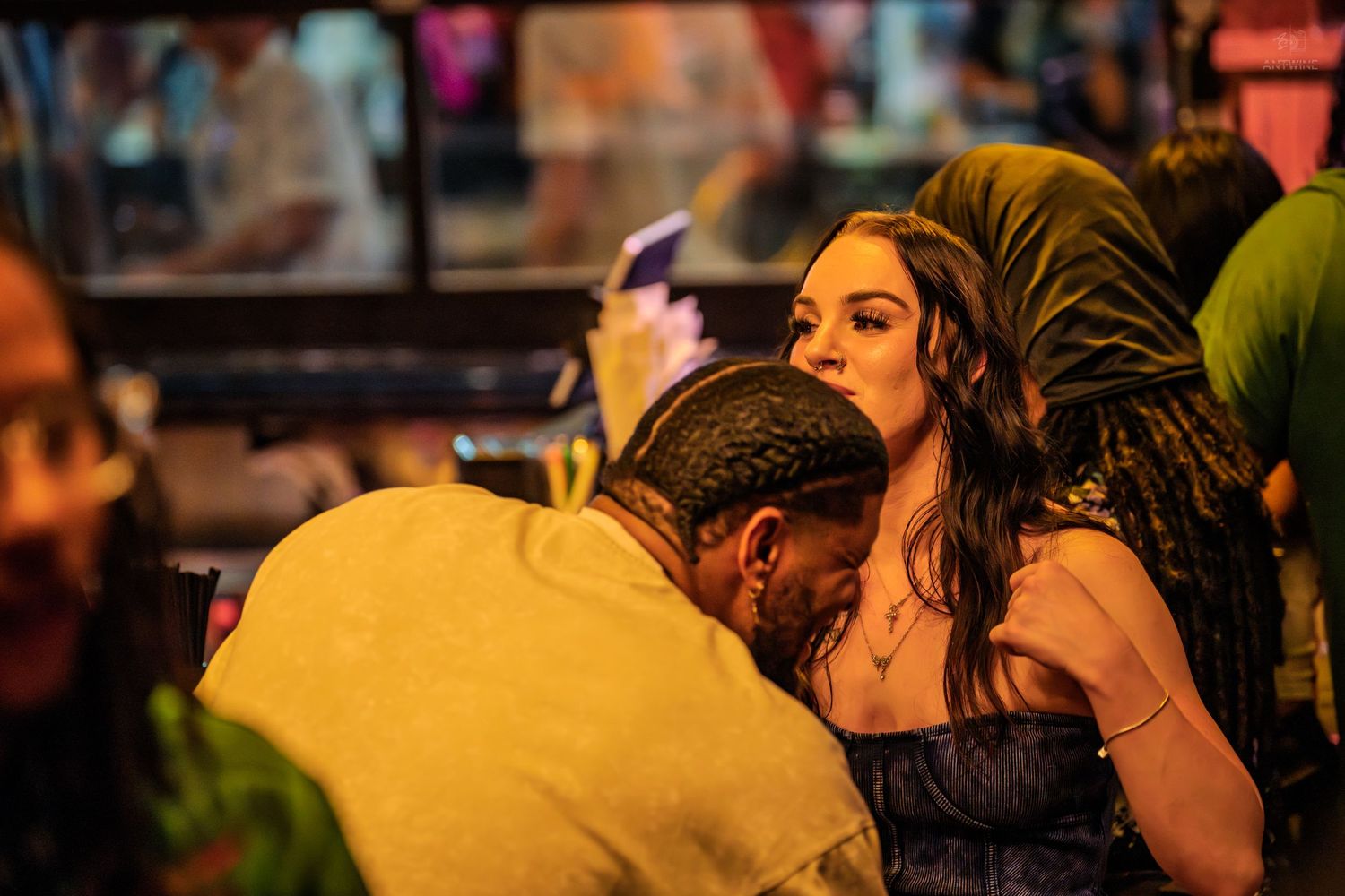 Young woman in strapless dress socializing at a lively bar with friends in colorful nightlife setting.