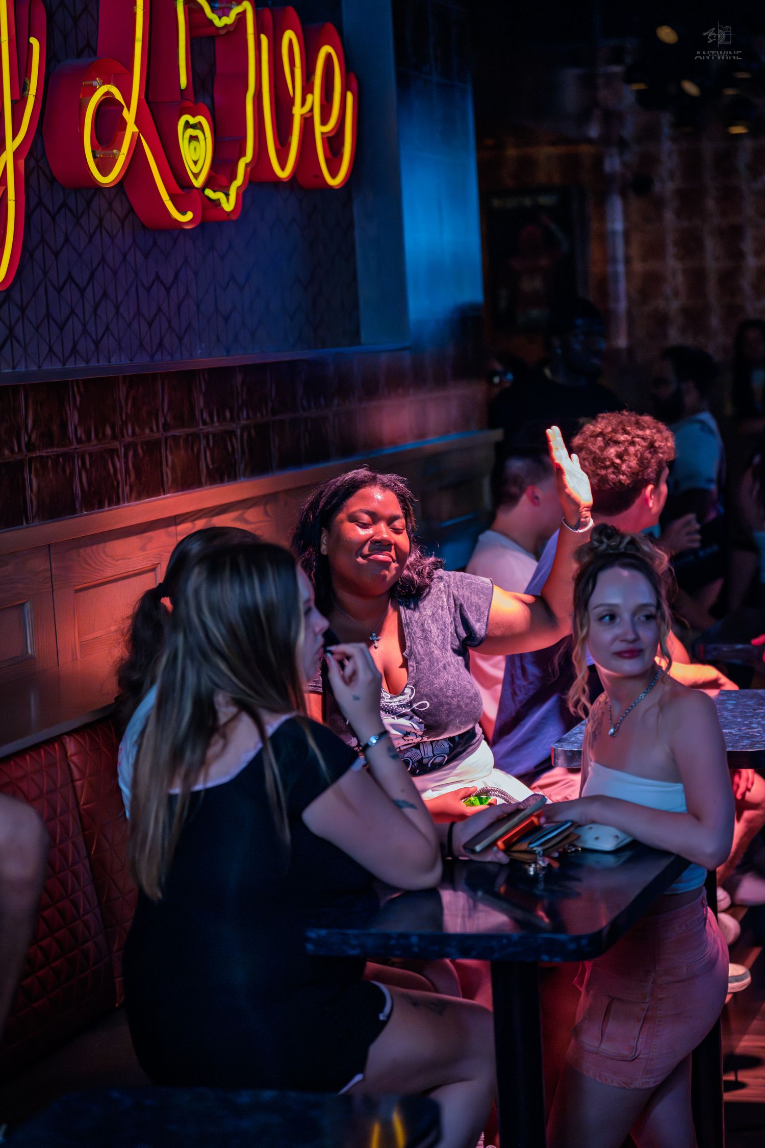 Group of women laugh and socialize under neon signs at a bar.