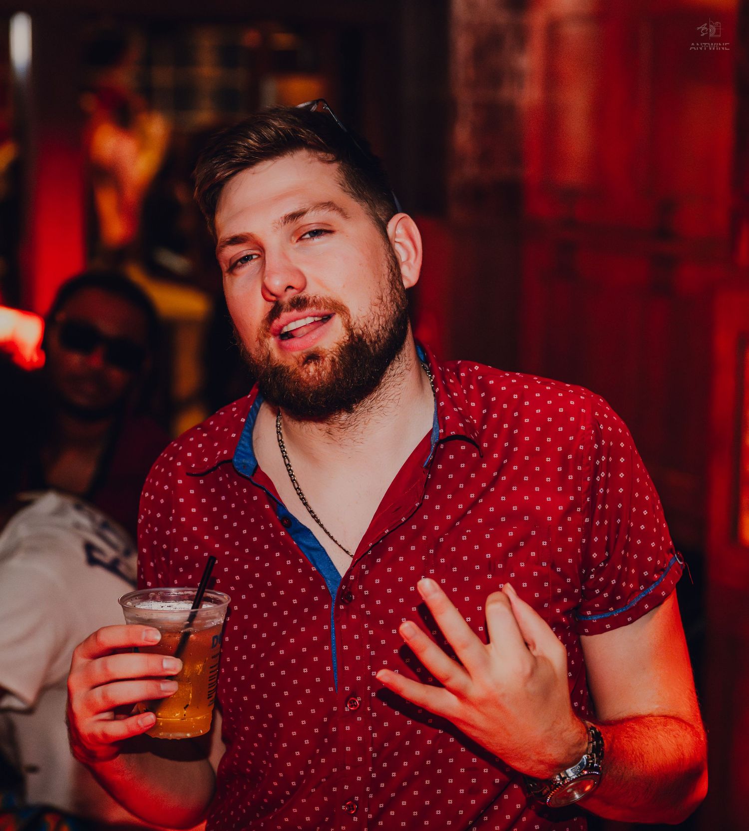 Man in red polka dot shirt holding a drink at a nightclub event.