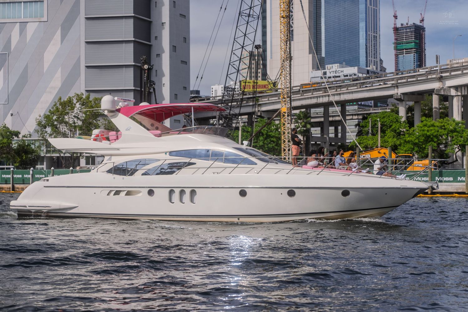 A sleek white luxury yacht cruising on a river with a city skyline and crane in the background.