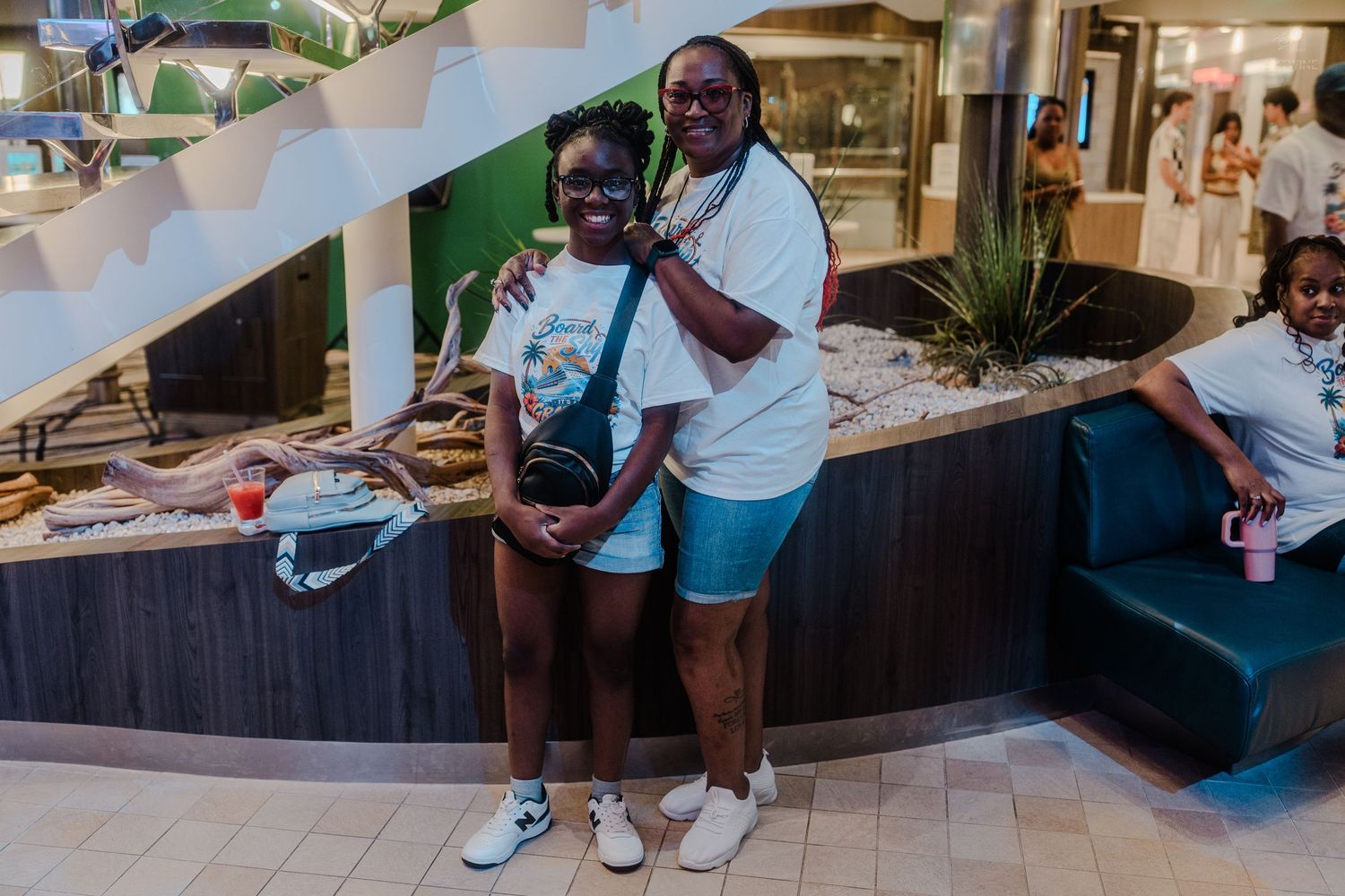 Two women in white outfits pose together smiling inside a bright cruise ship interior.