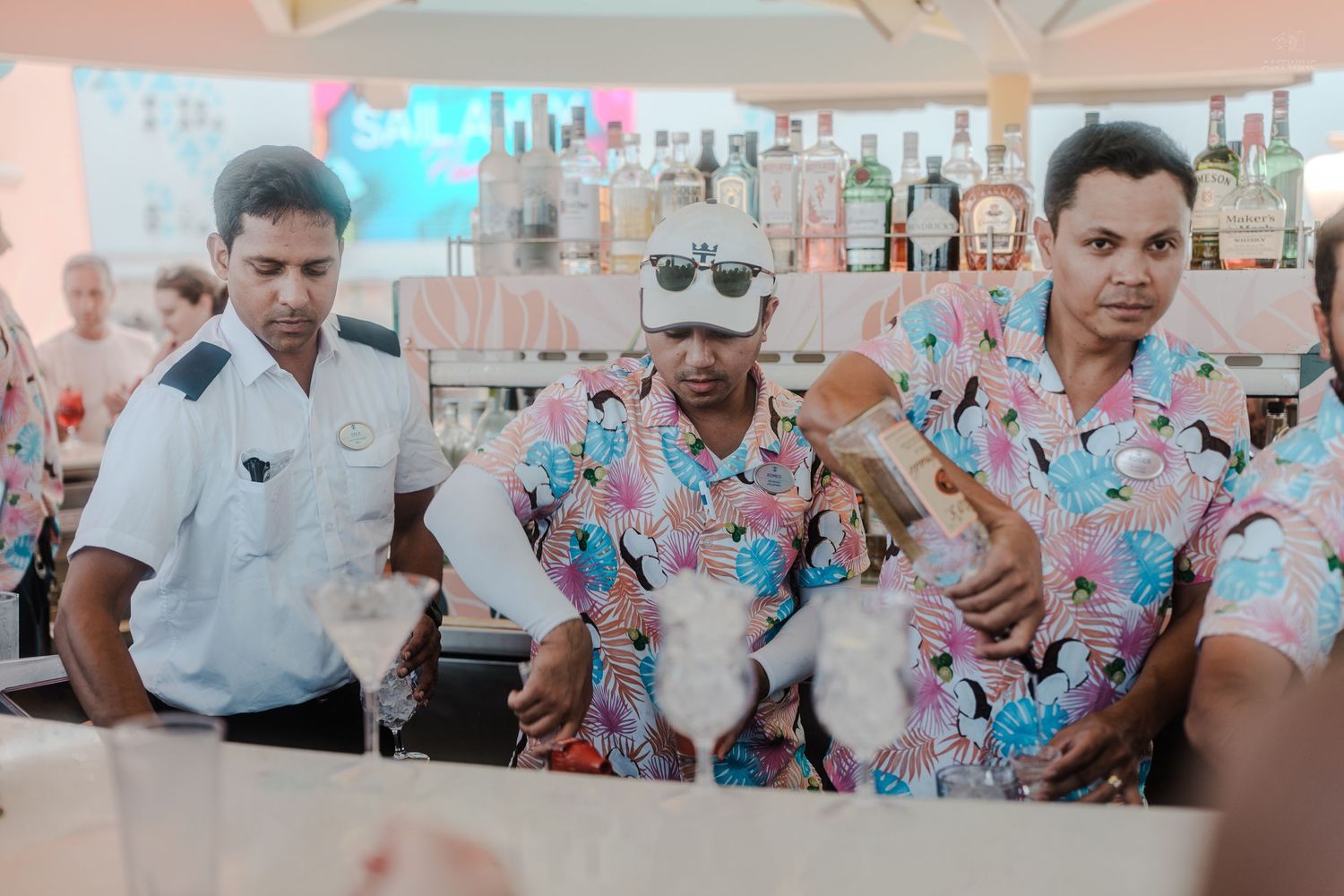 Three bartenders in colorful floral shirts shaking cocktails at an outdoor beach bar.