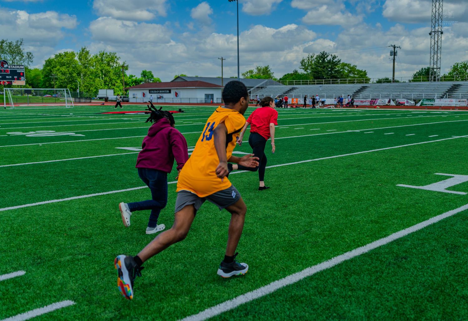 Students running drills on a green turf football field during an outdoor sports activity on a cloudy day.