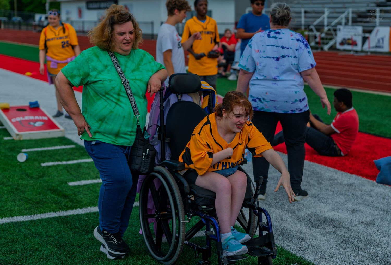 Volunteer pushes athlete in wheelchair at Special Olympics track event on red turf field.