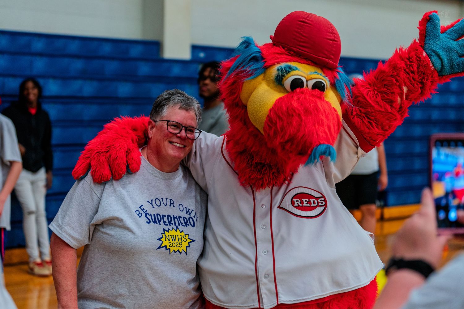Woman posing with Cincinnati Reds mascot Mr. Redlegs in a gymnasium, both smiling for a photo.