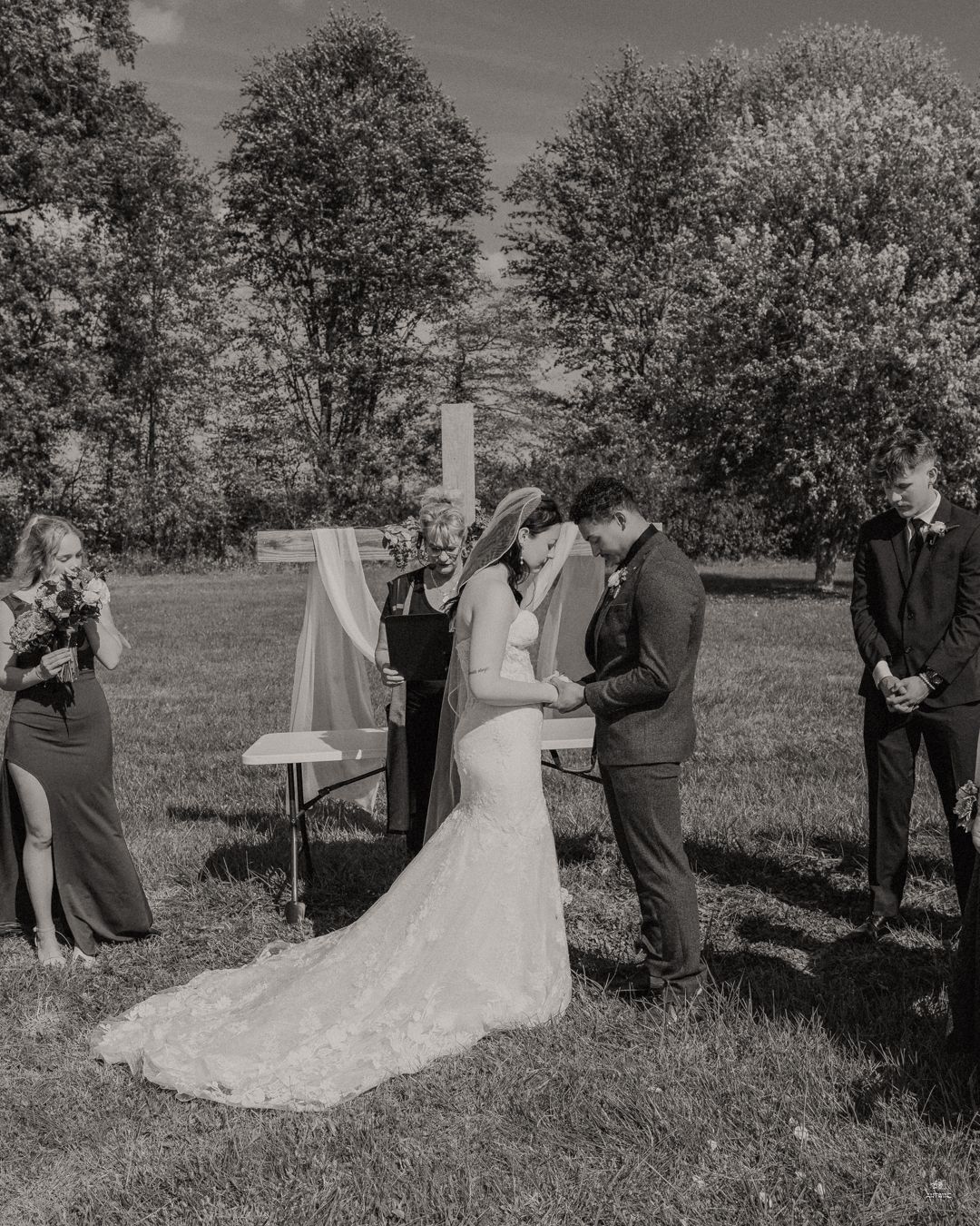 Black and white outdoor wedding ceremony with bride and groom at altar surrounded by guests.