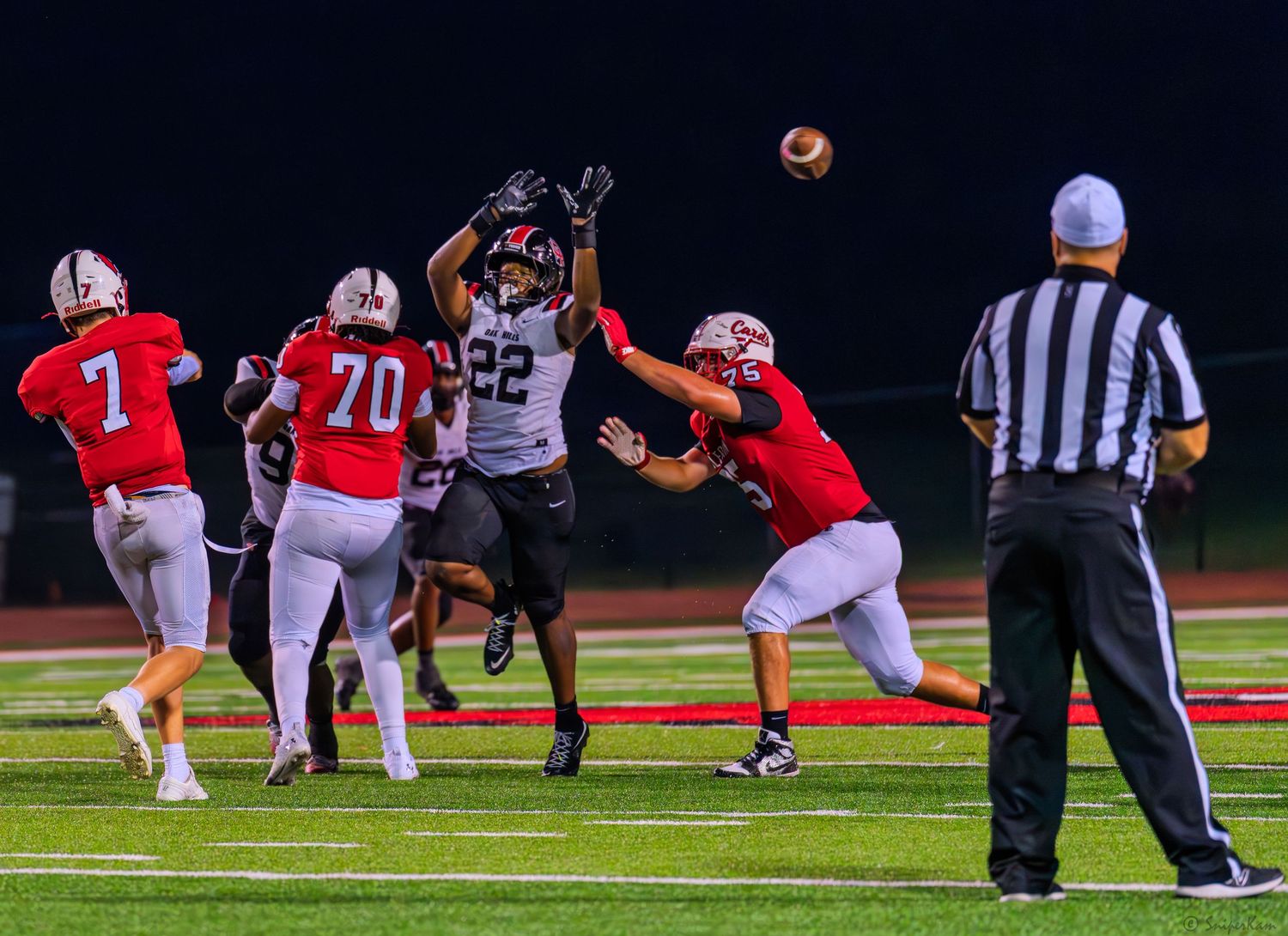 A football player in black jersey #22 leaps to catch a pass while defenders in red uniforms attempt to block during a night game.