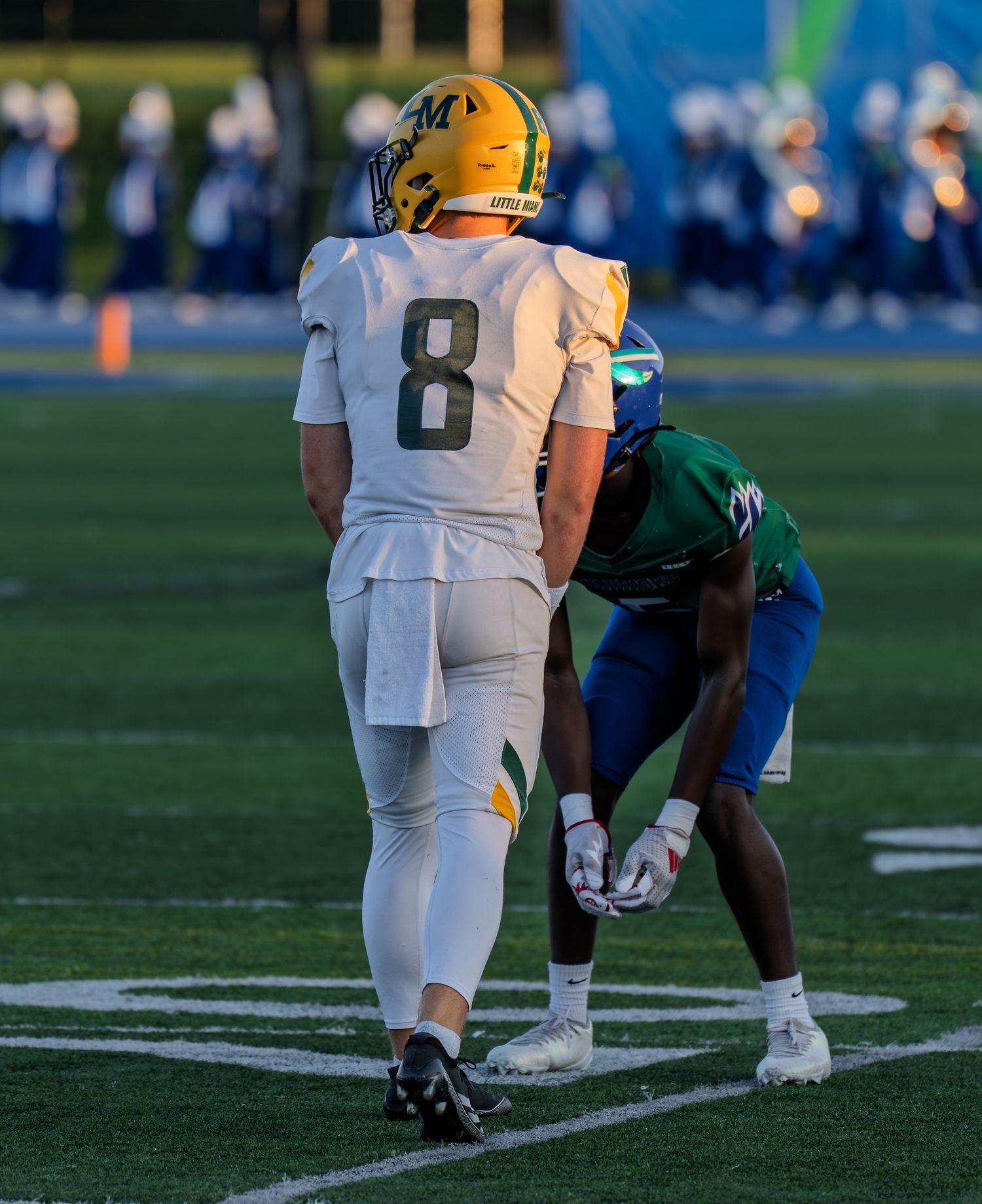 Player number 8 in white uniform stands as Warriors defender crouches in position during a football game.