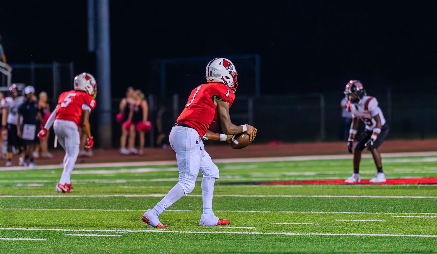 Colerain Cardinals quarterback prepares to throw during a night high school football game on red turf.