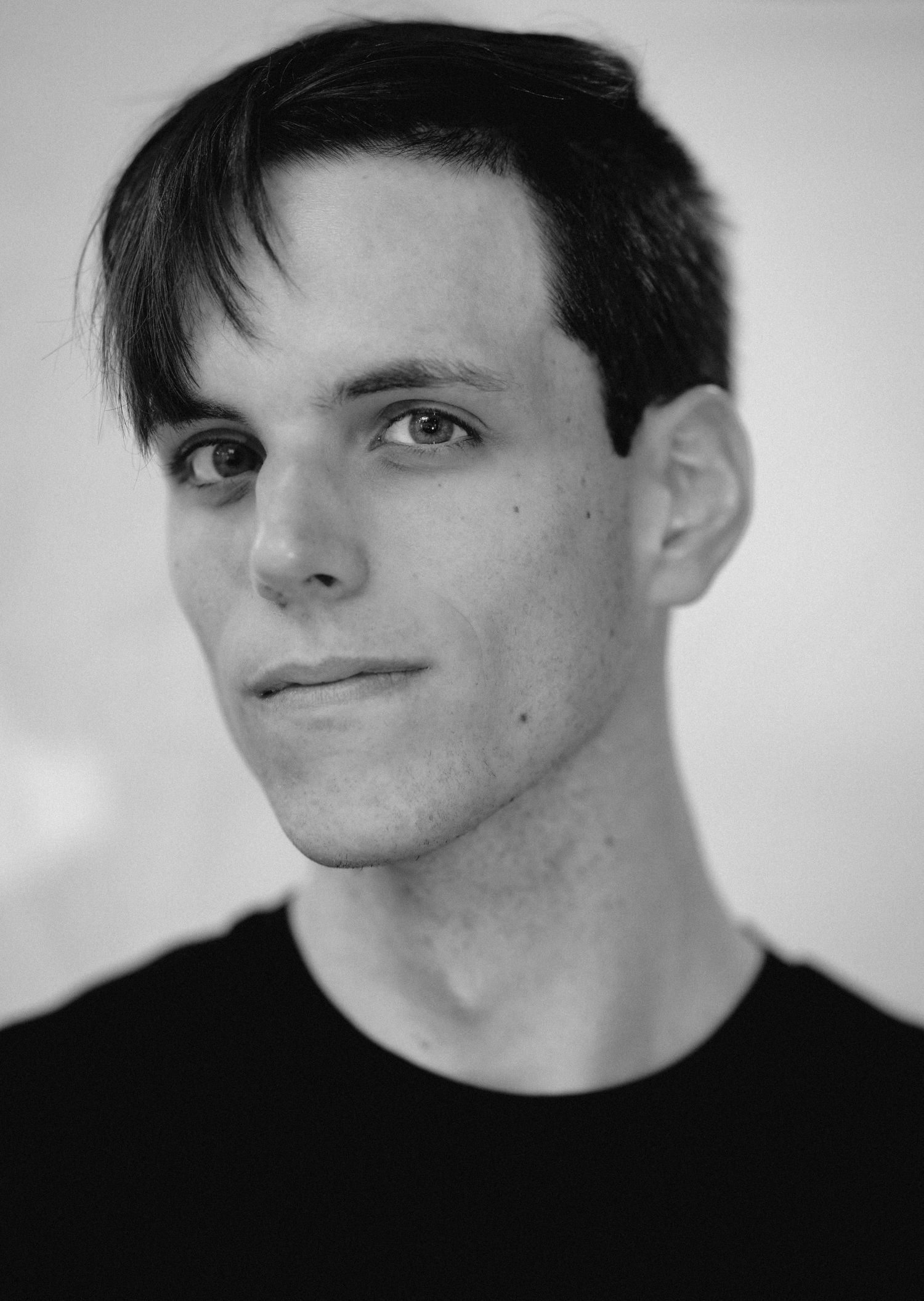 Black and white close-up portrait of a young man with dark hair and sharp facial features.