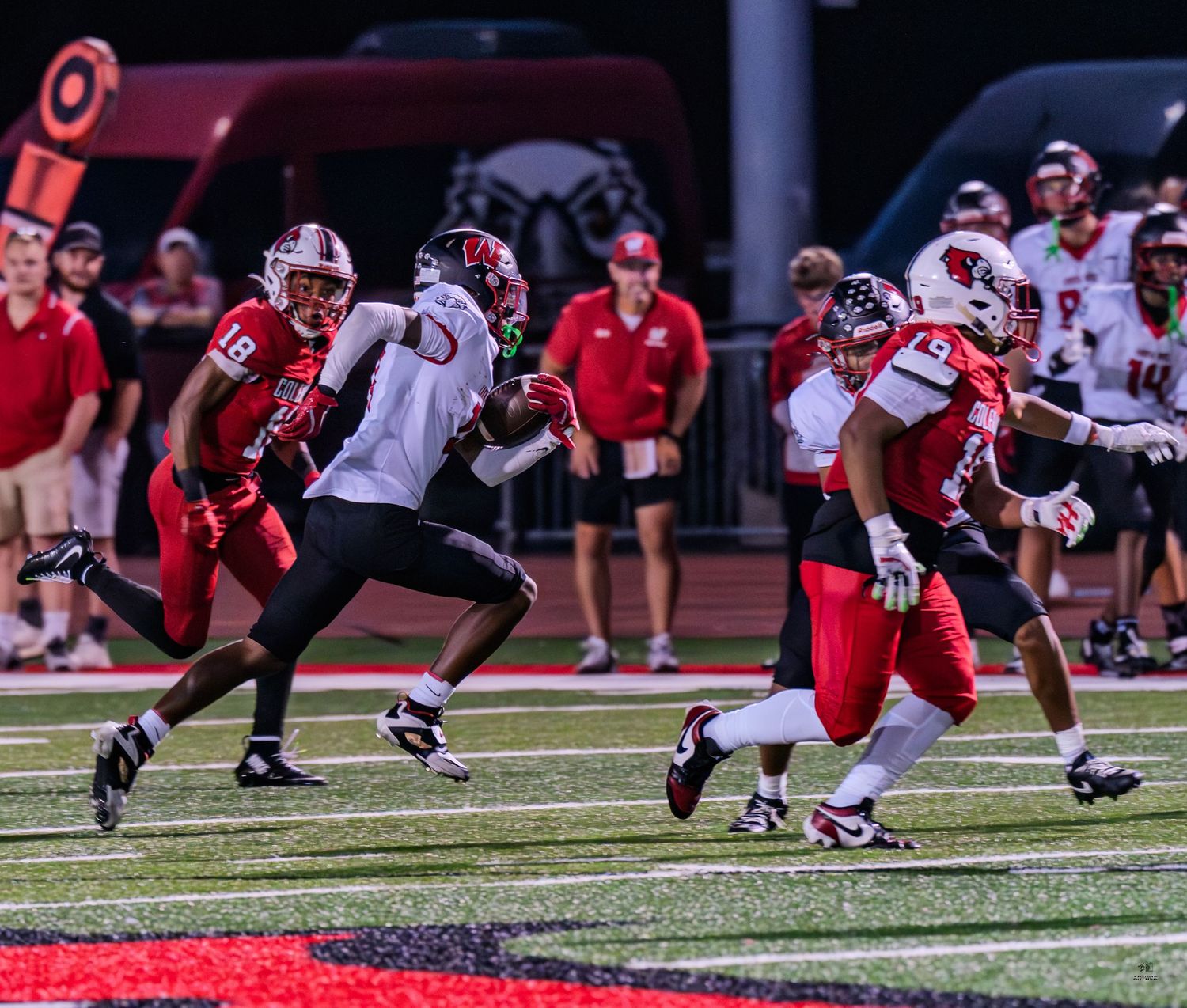 Red team defenders pursue a ball carrier in white during a competitive high school football game.