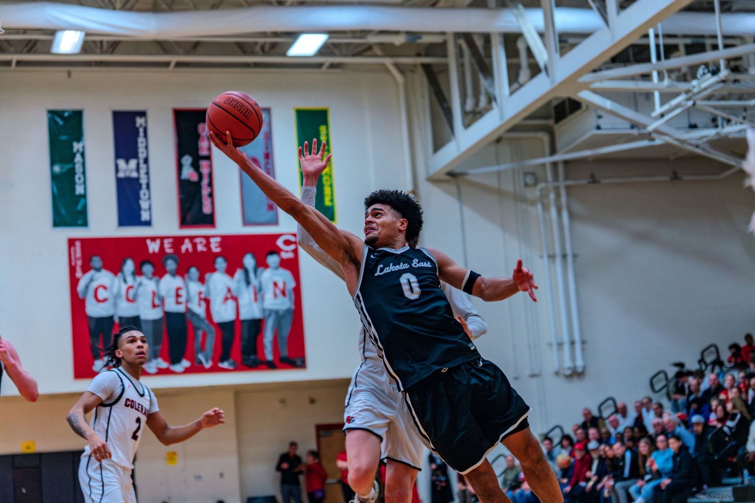 A basketball player in jersey number 0 leaps for a layup during an indoor high school game.