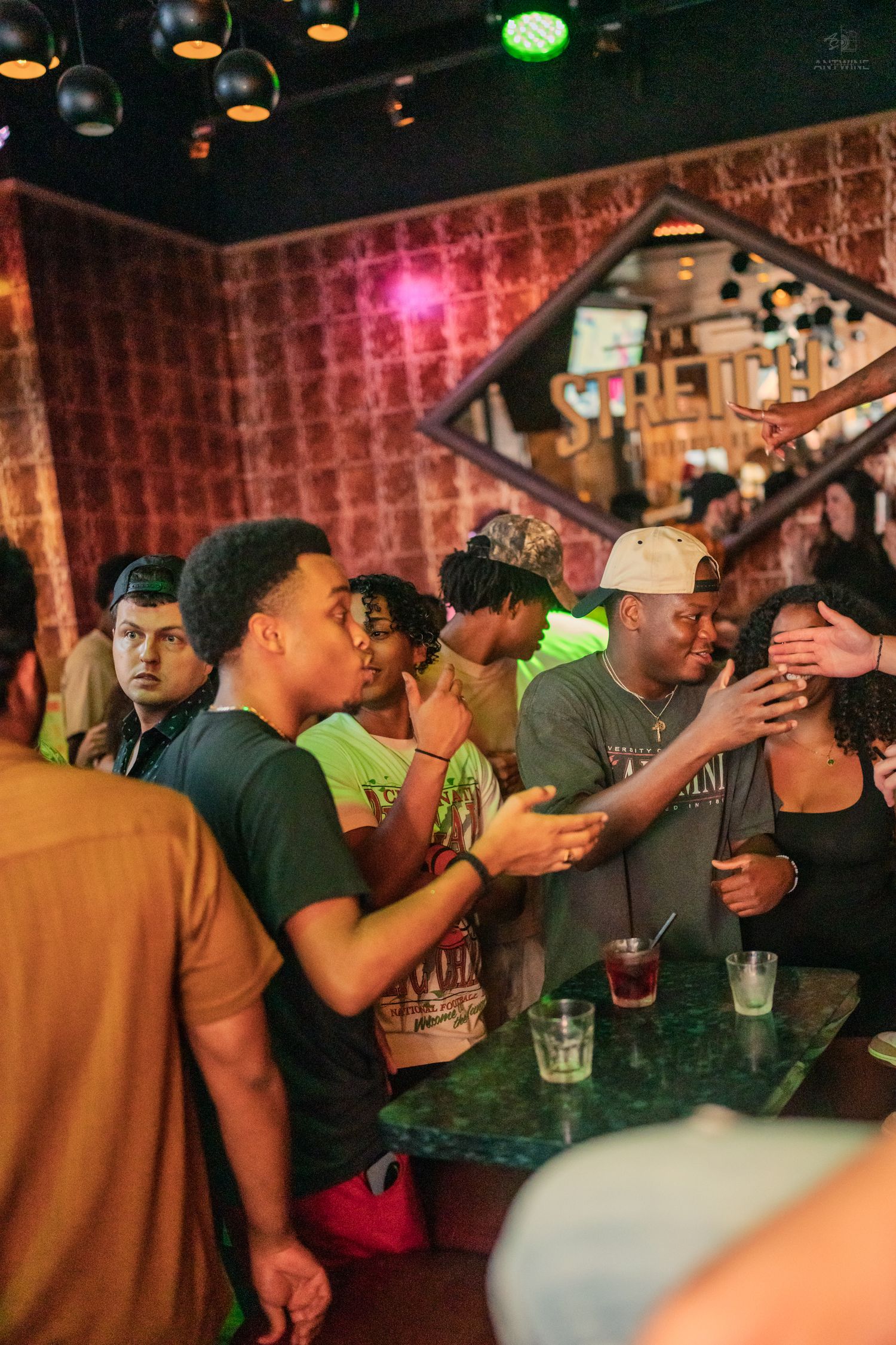Young adults gathered around a bar counter enjoying drinks at a dimly lit nightclub.