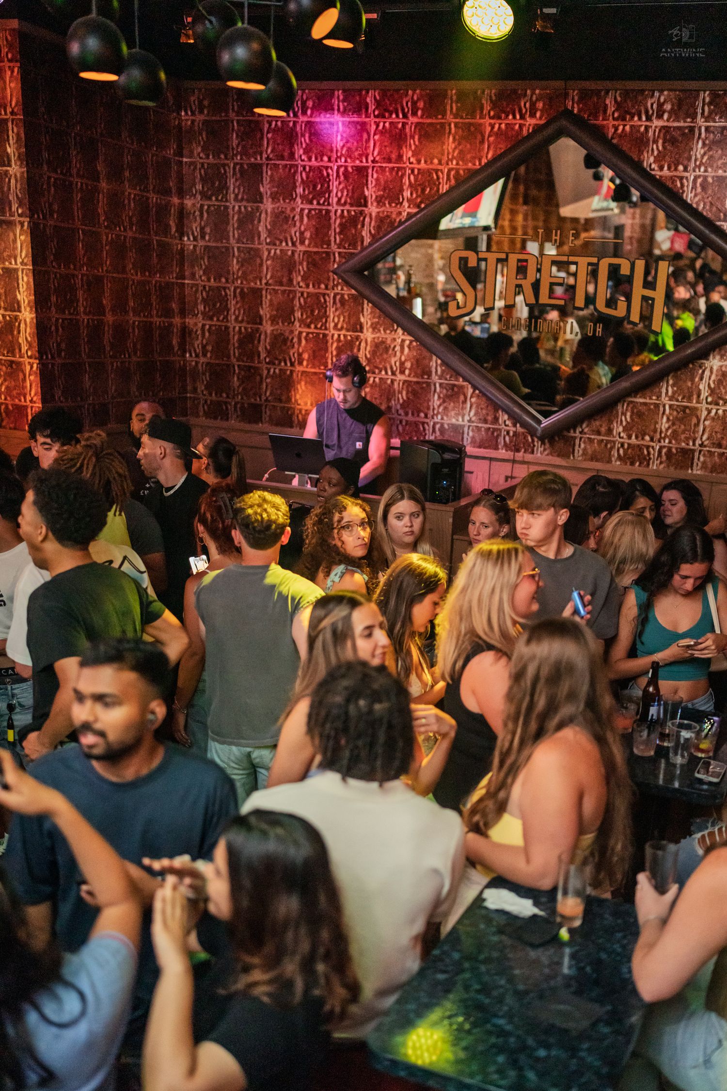 Packed nightclub crowd dancing under yellow-green lights below Stretch bar sign.