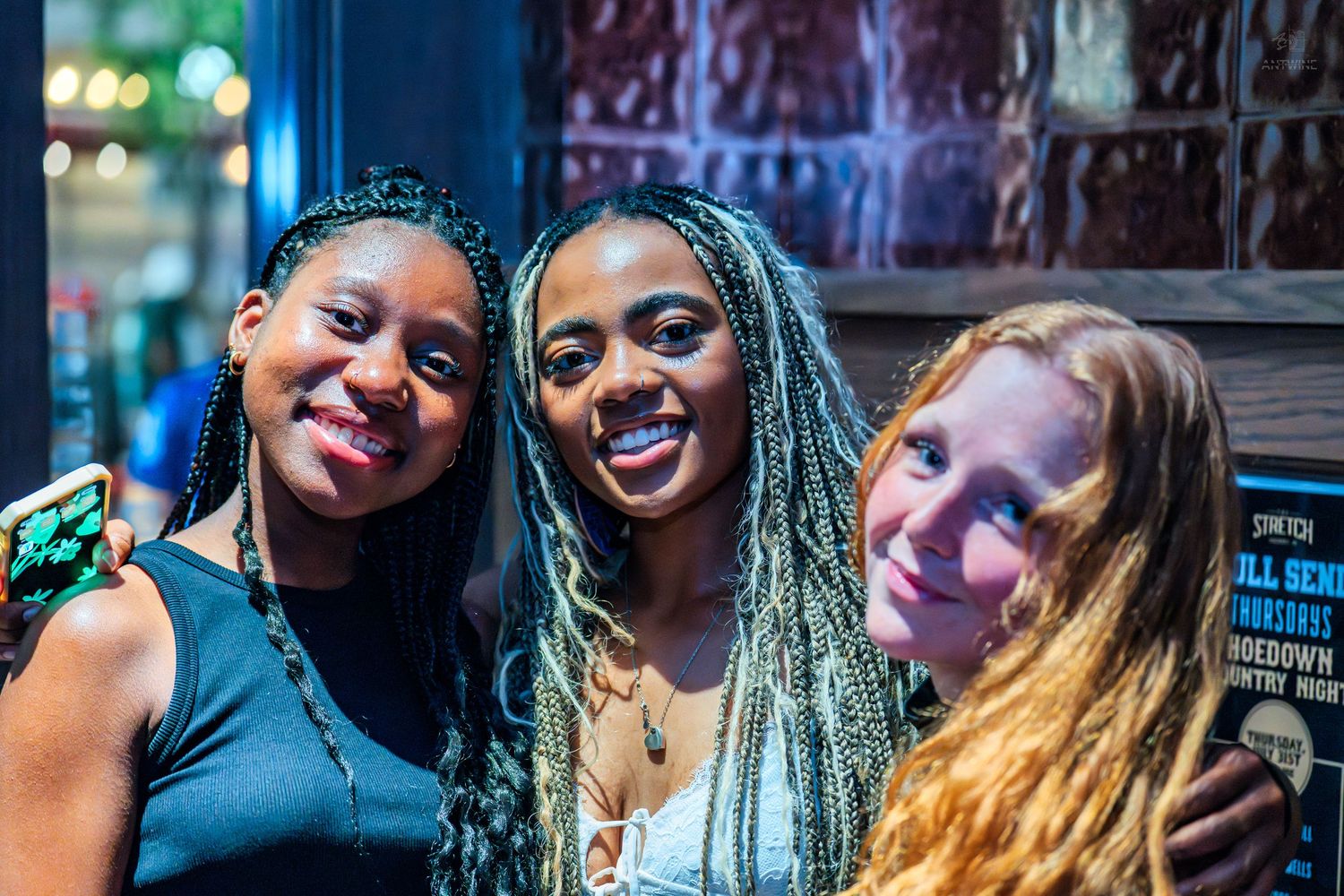 Three happy women posing closely together at an indoor nightlife event.