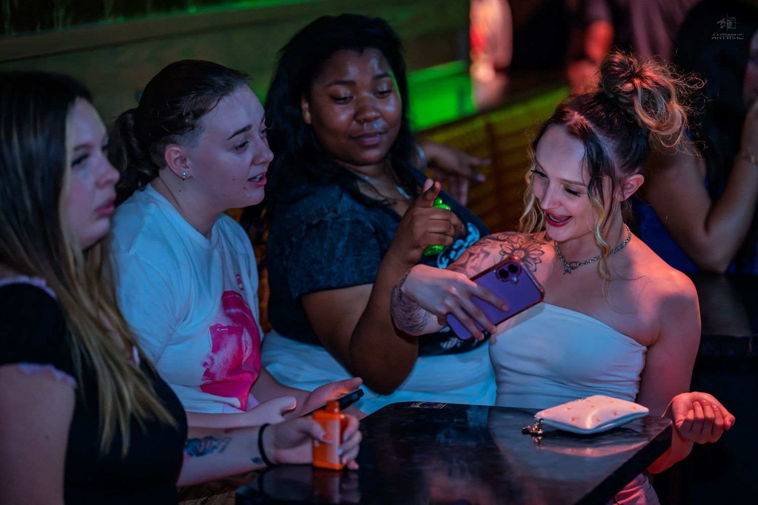 Four women socializing and sharing drinks at a colorful nightclub venue.