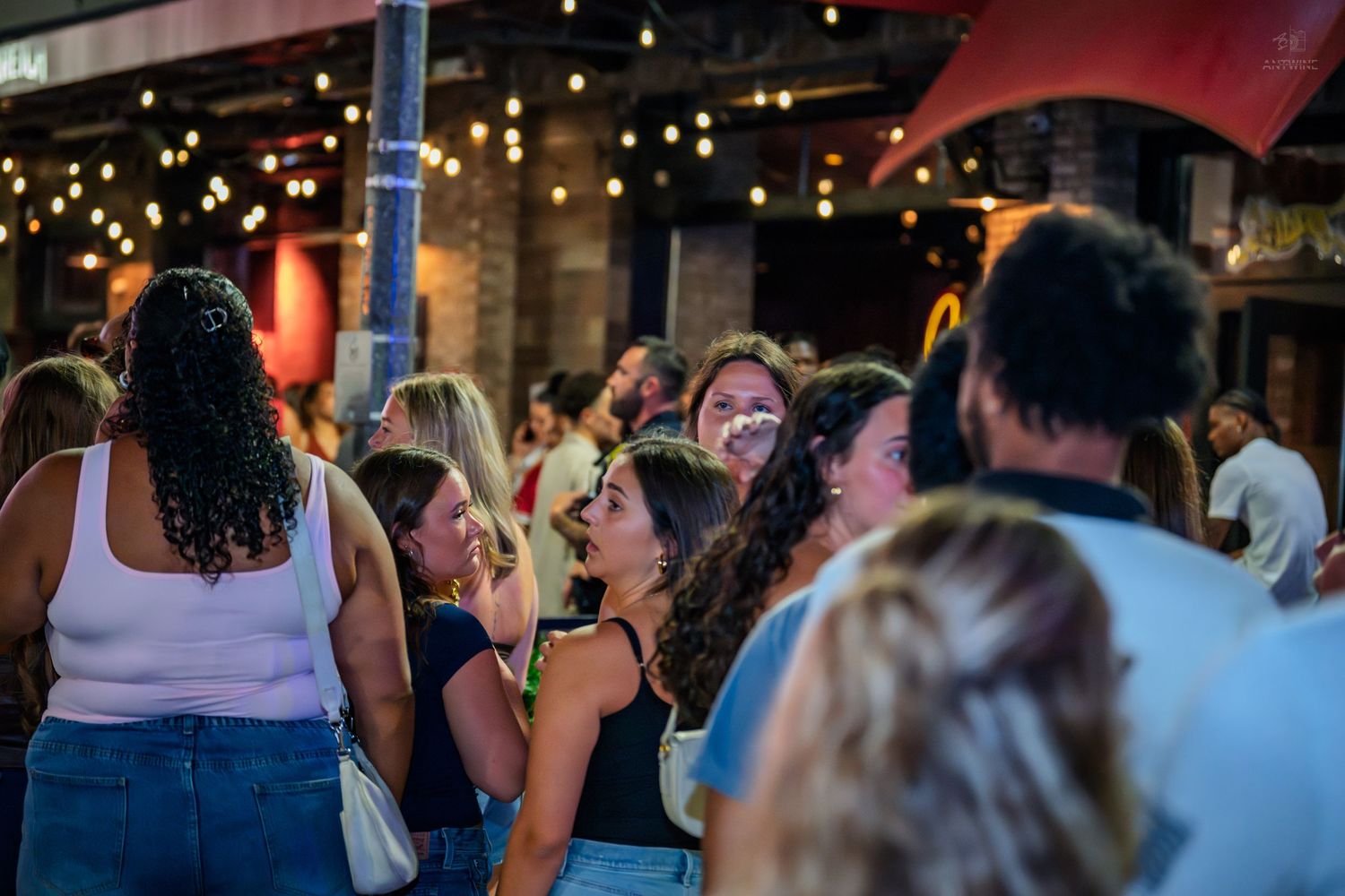 Group of young women socializing at an outdoor bar with string lights.