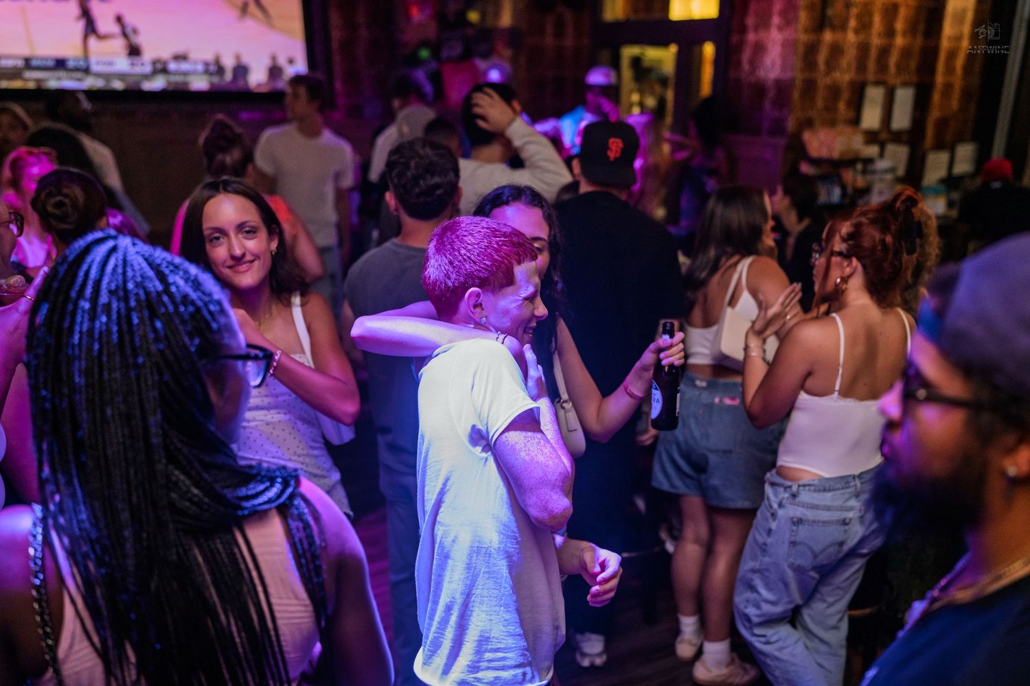 Smiling woman with braids enjoys a night out dancing with friends under purple club lights.
