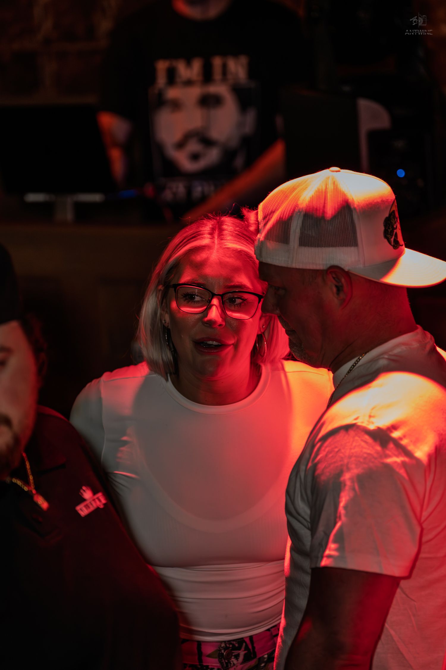 Couple sharing a close moment under red lighting at a lively nightclub event.
