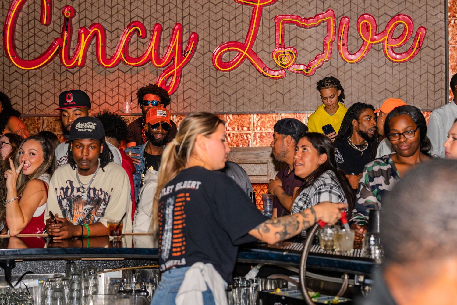Crowd of people gathered at a bar under a Cincy Love neon sign.