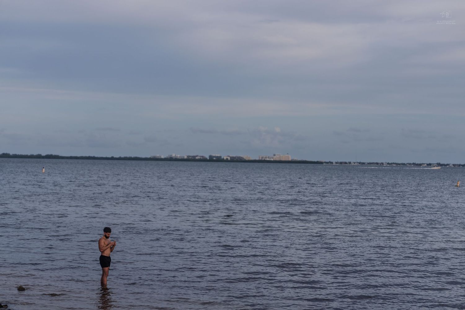 Person wading in shallow water at Key Biscayne bay under cloudy skies with city skyline in distance.
