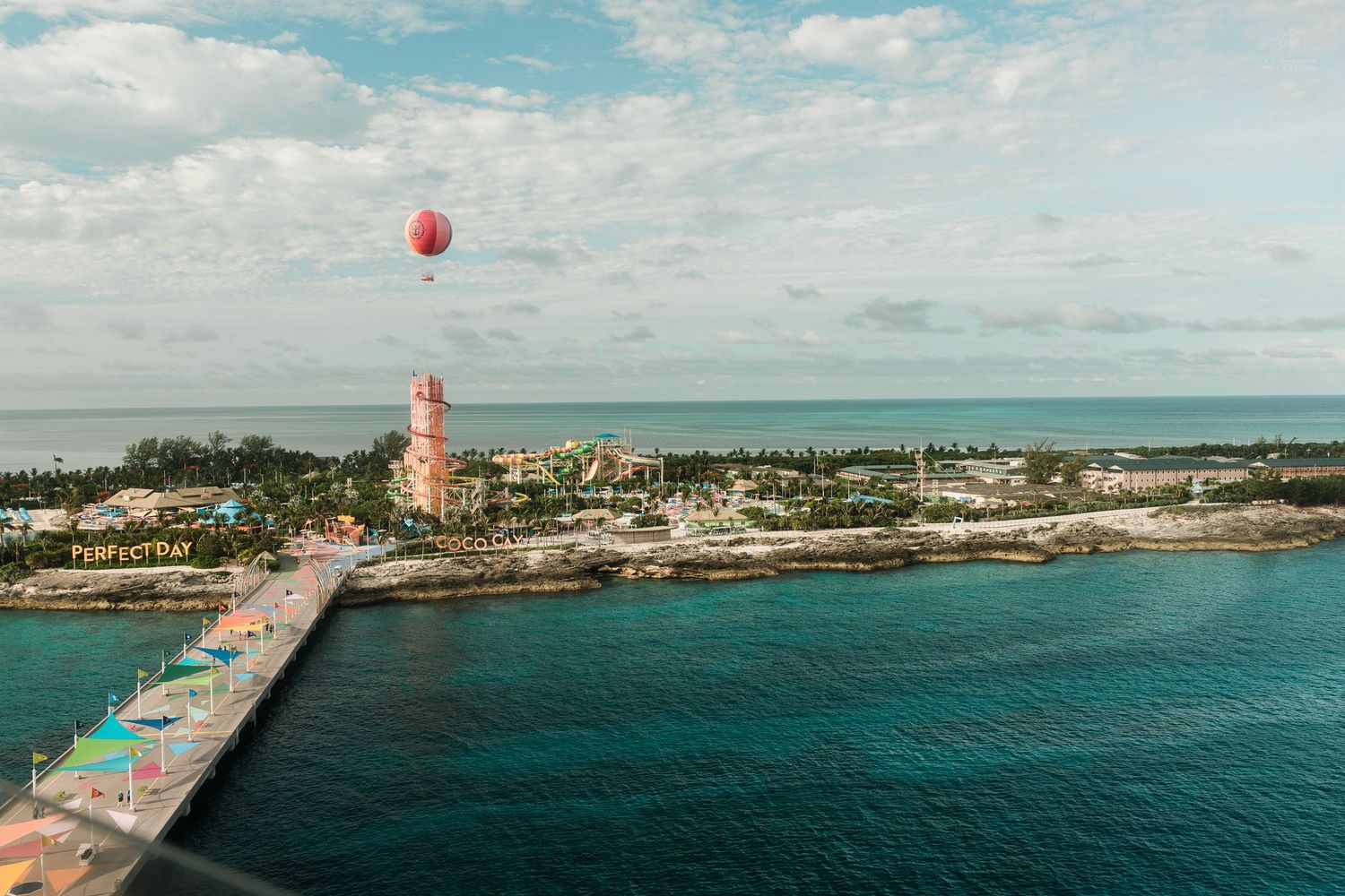 Aerial view of a tropical island port with a red hot air balloon and lighthouse.