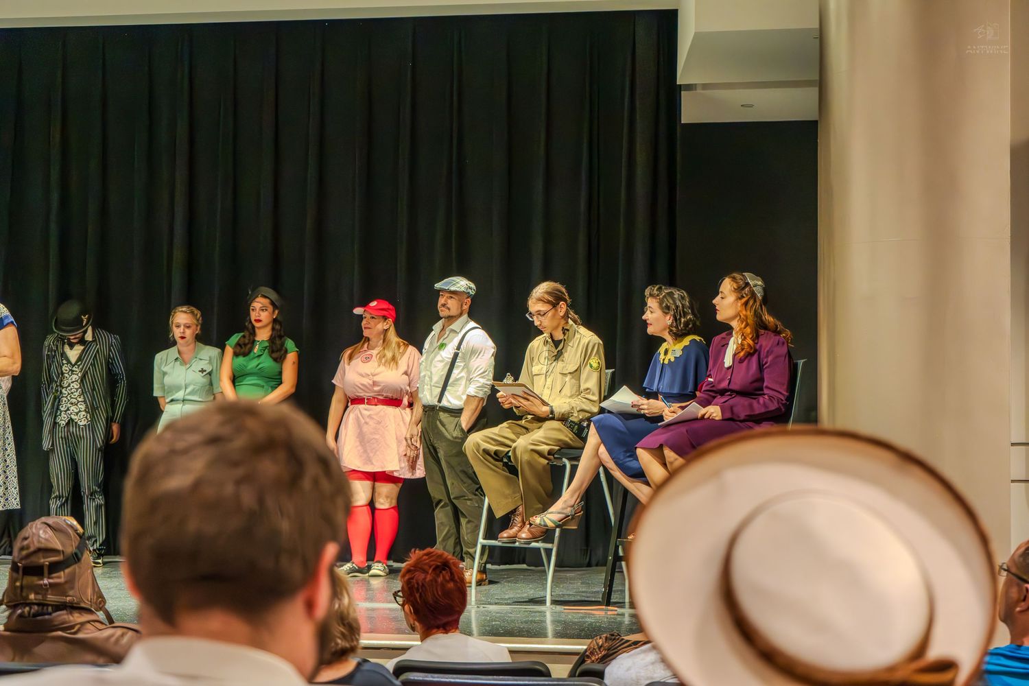 Theater performers in colorful costumes on stage during a dramatic group scene at a community play production.