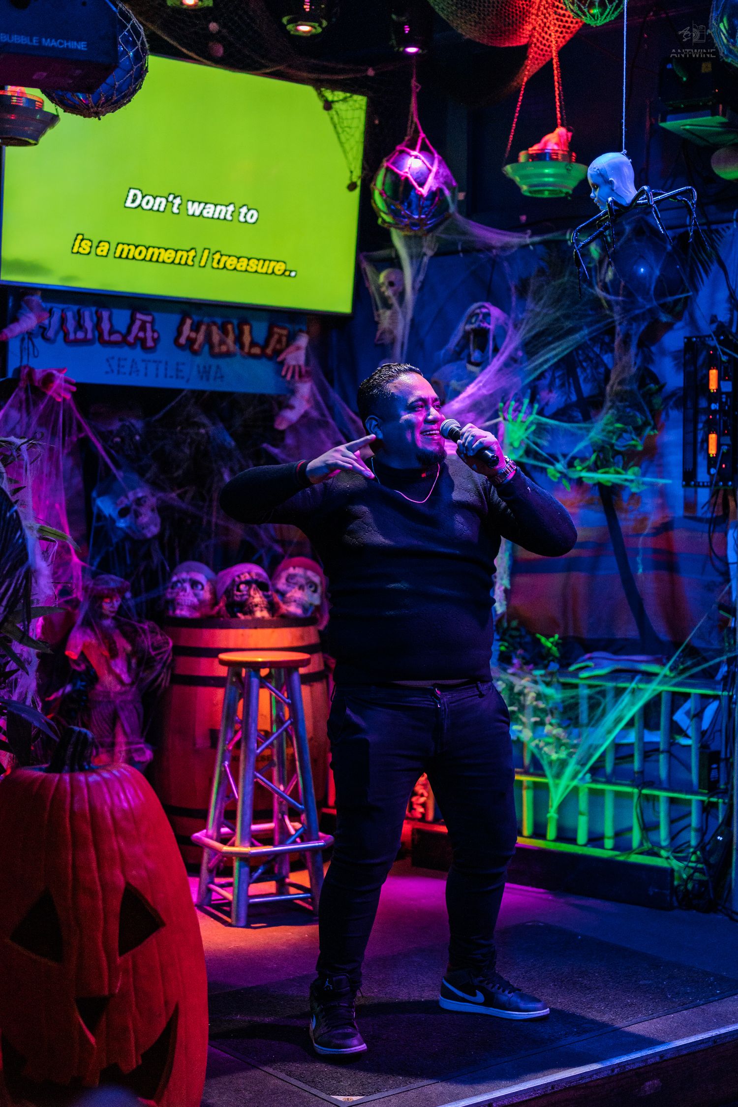 Man singing karaoke on a Halloween-themed stage with green screen lyrics and festive decor.