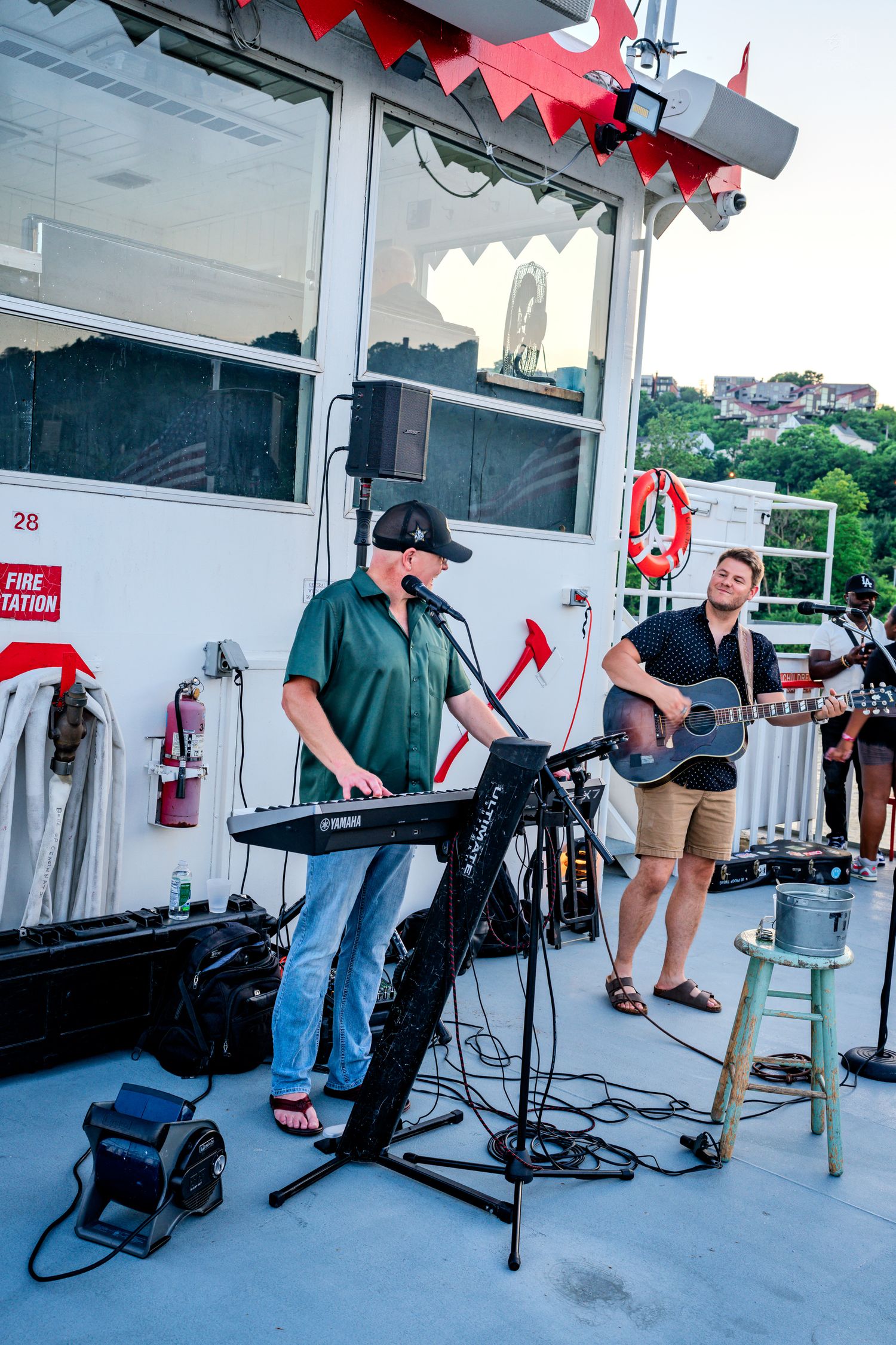 Musician playing Yamaha keyboard at outdoor deck concert on a riverboat at dusk.