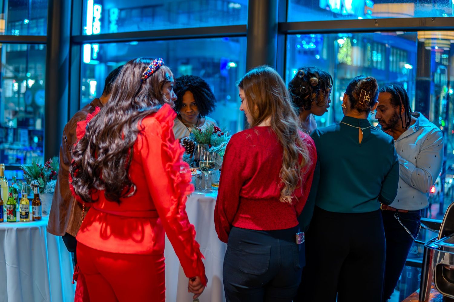 Group of women in elegant attire socializing at an upscale evening event near large windows.