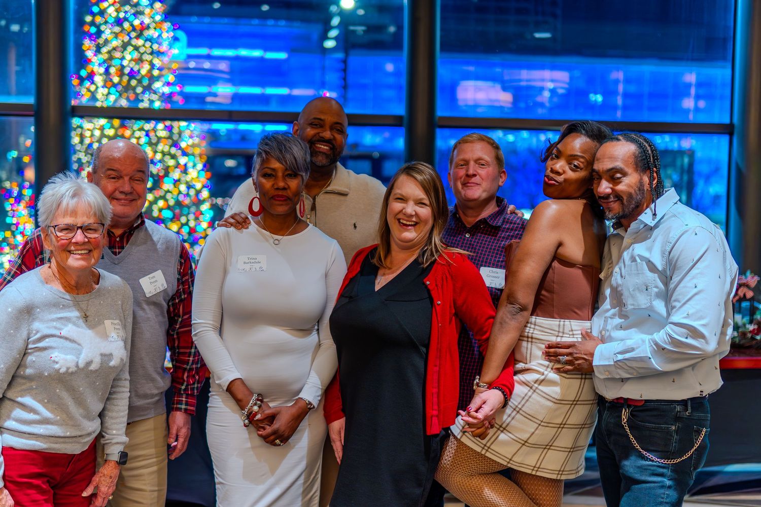Group of diverse adults smiling together at a festive holiday party with a decorated Christmas tree in the background.