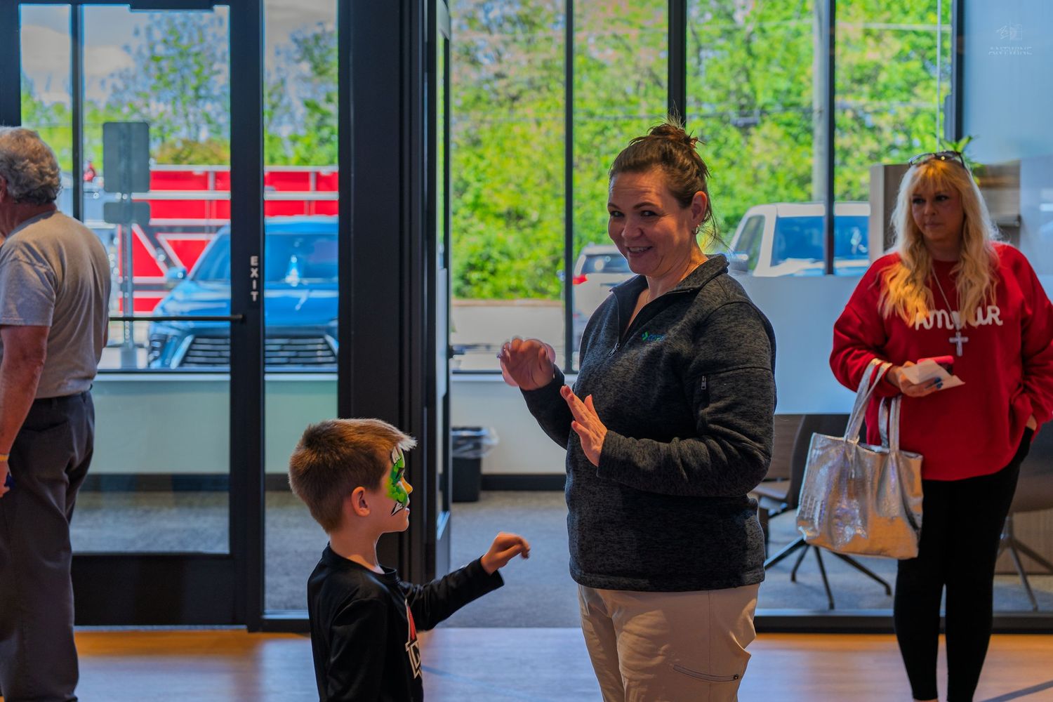 Woman interacting with a young boy wearing green sunglasses inside a modern building lobby.