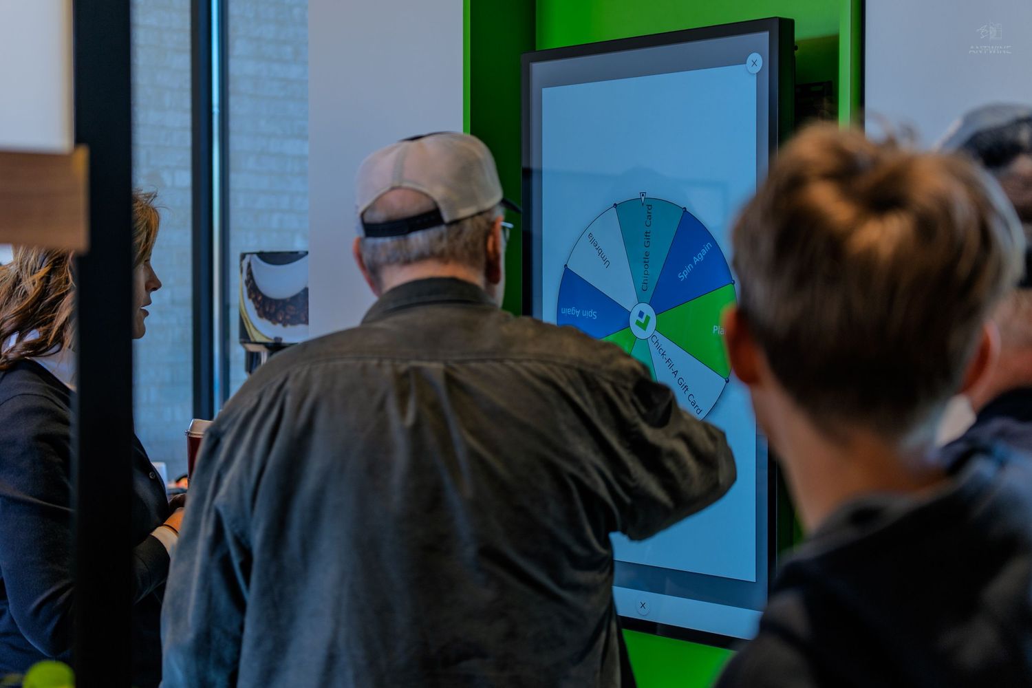 People gathered around a colorful interactive wheel display on a green digital screen at an indoor event.