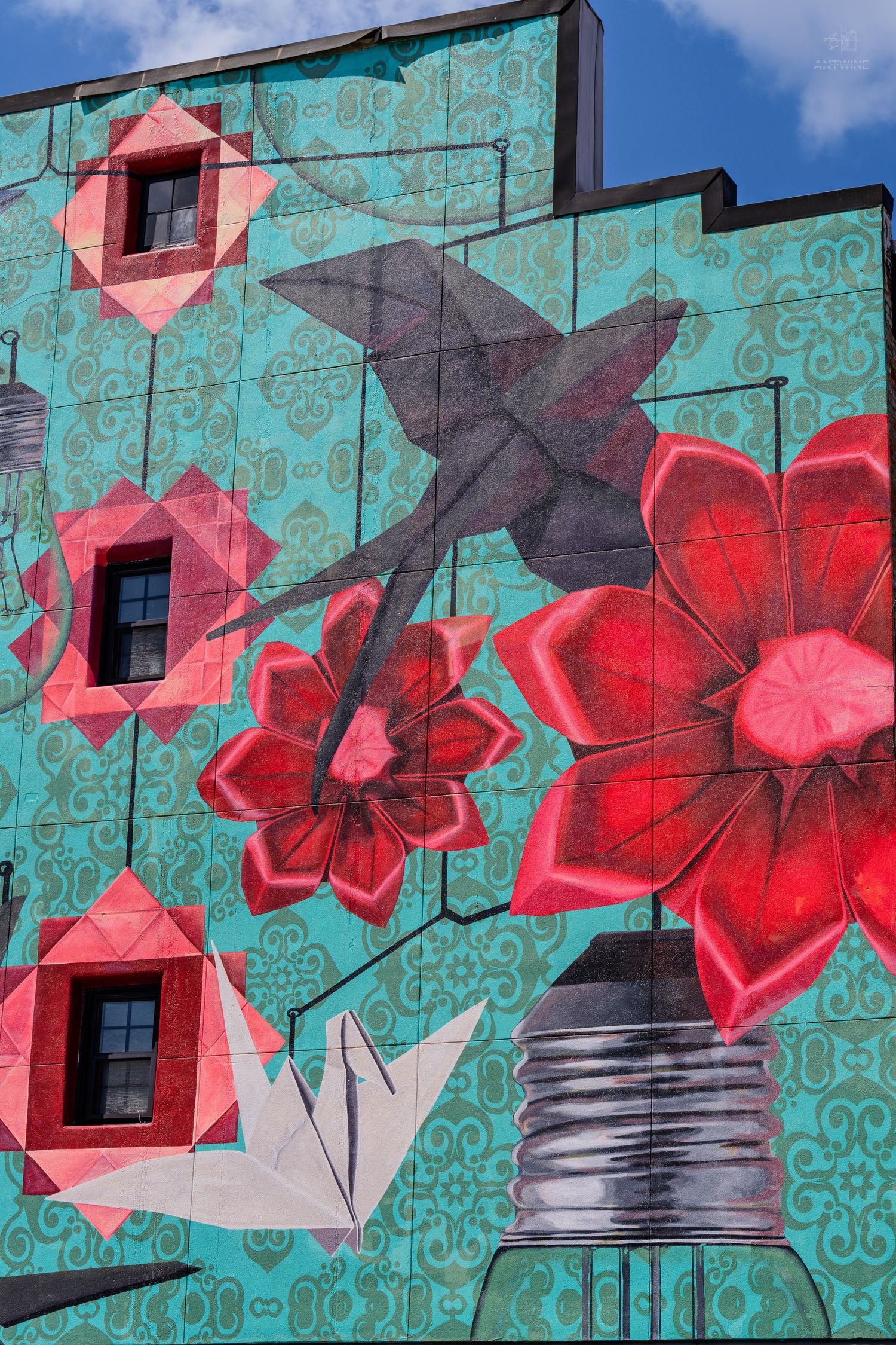 Vibrant street mural featuring origami birds and red flowers on a teal patterned wall of a building.