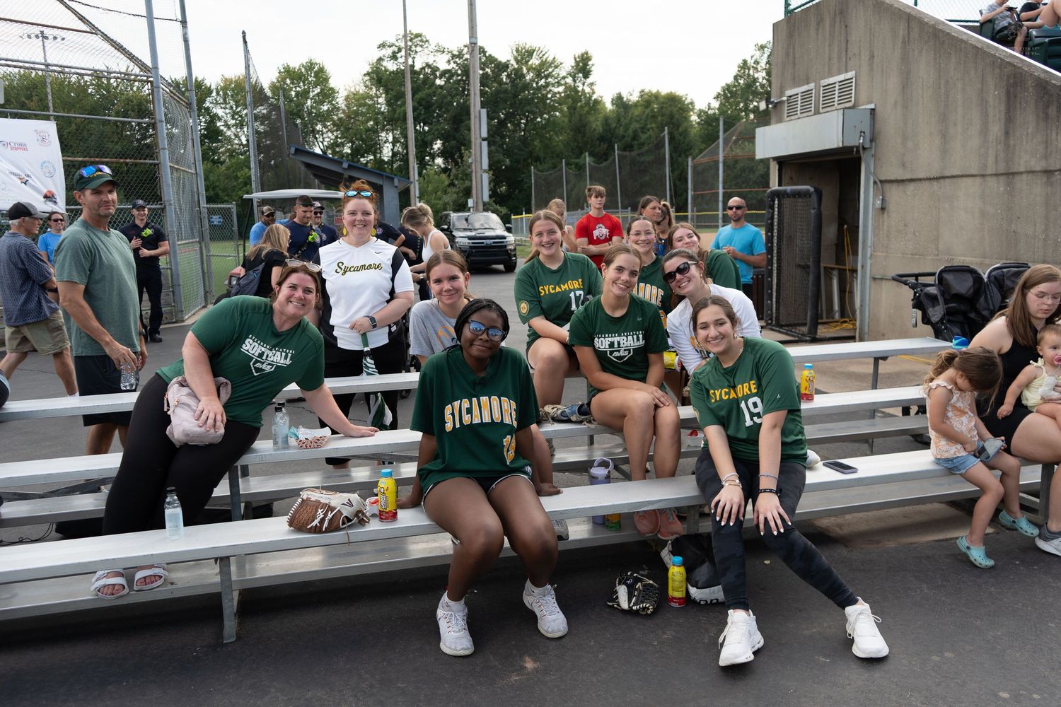 Group of young women in green Picayune jerseys posing on bleachers at an outdoor softball field.