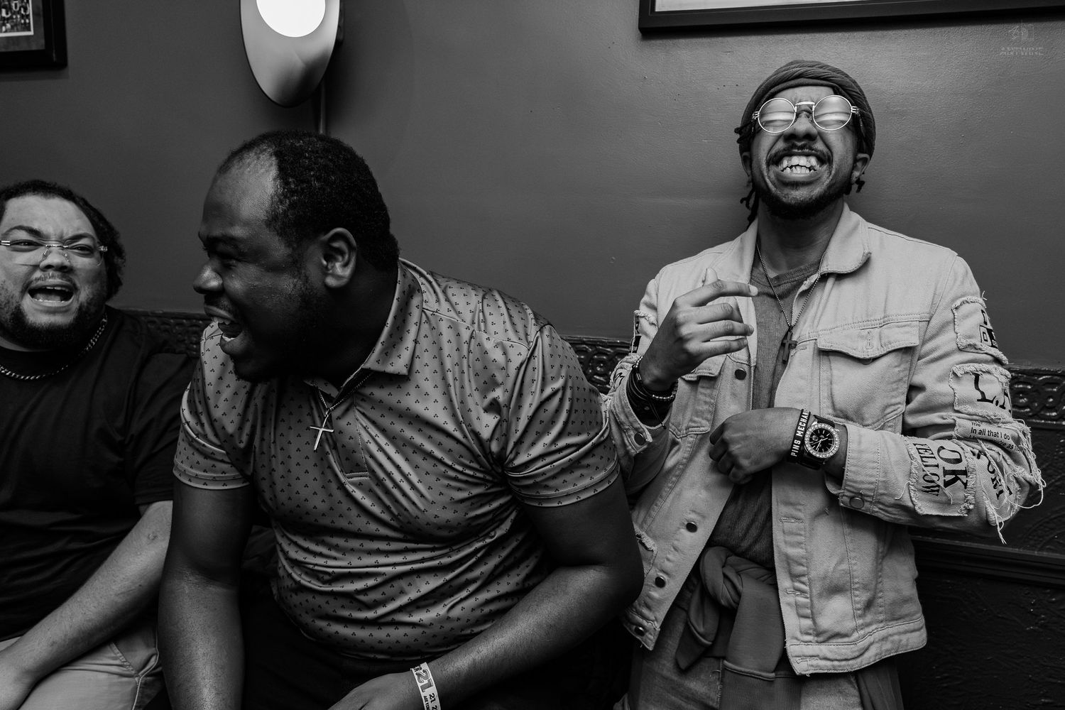 Three men laughing and enjoying themselves in a candid black and white photo taken indoors.