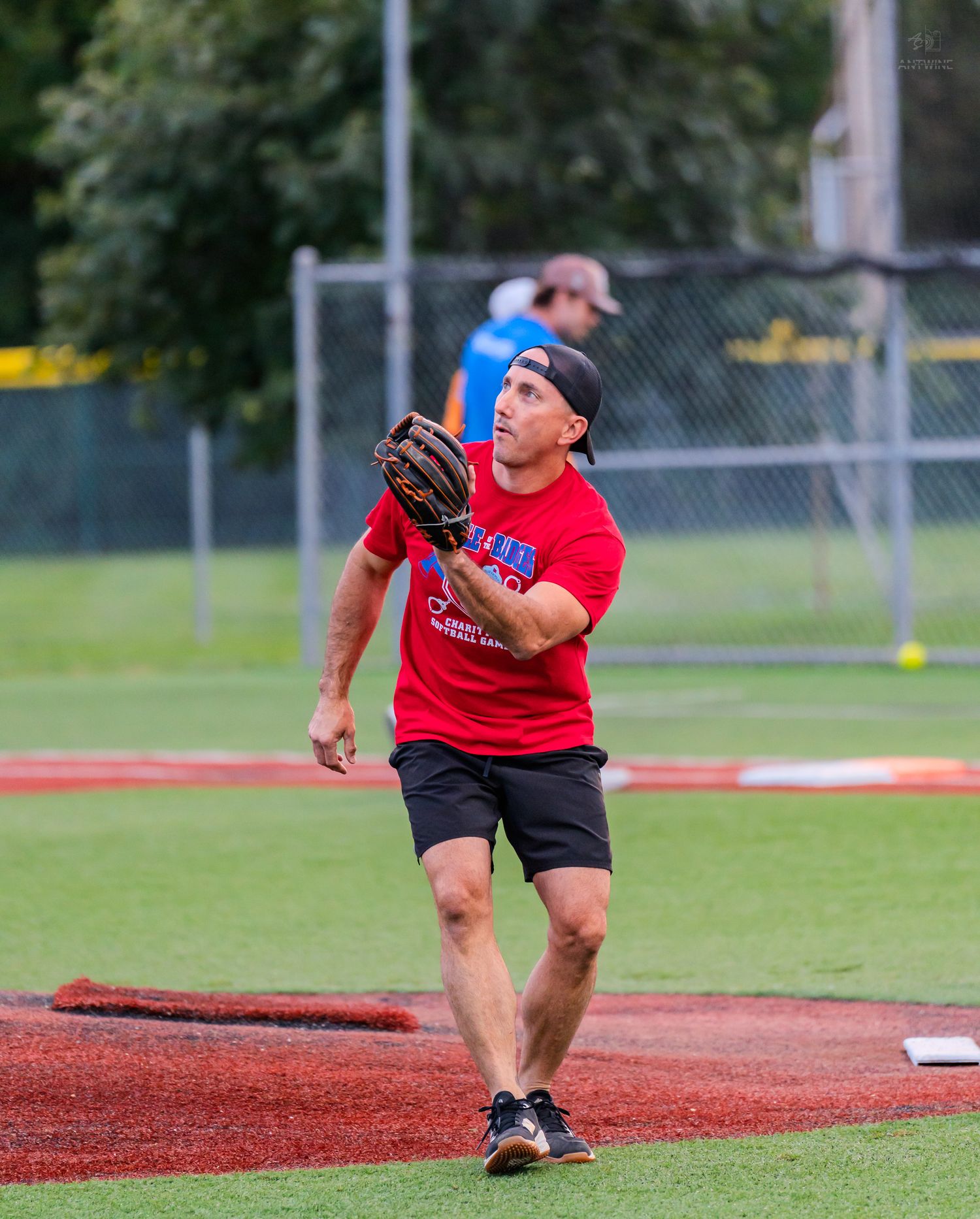 Athletic player in red shirt catching a softball with a glove on a recreational baseball field.