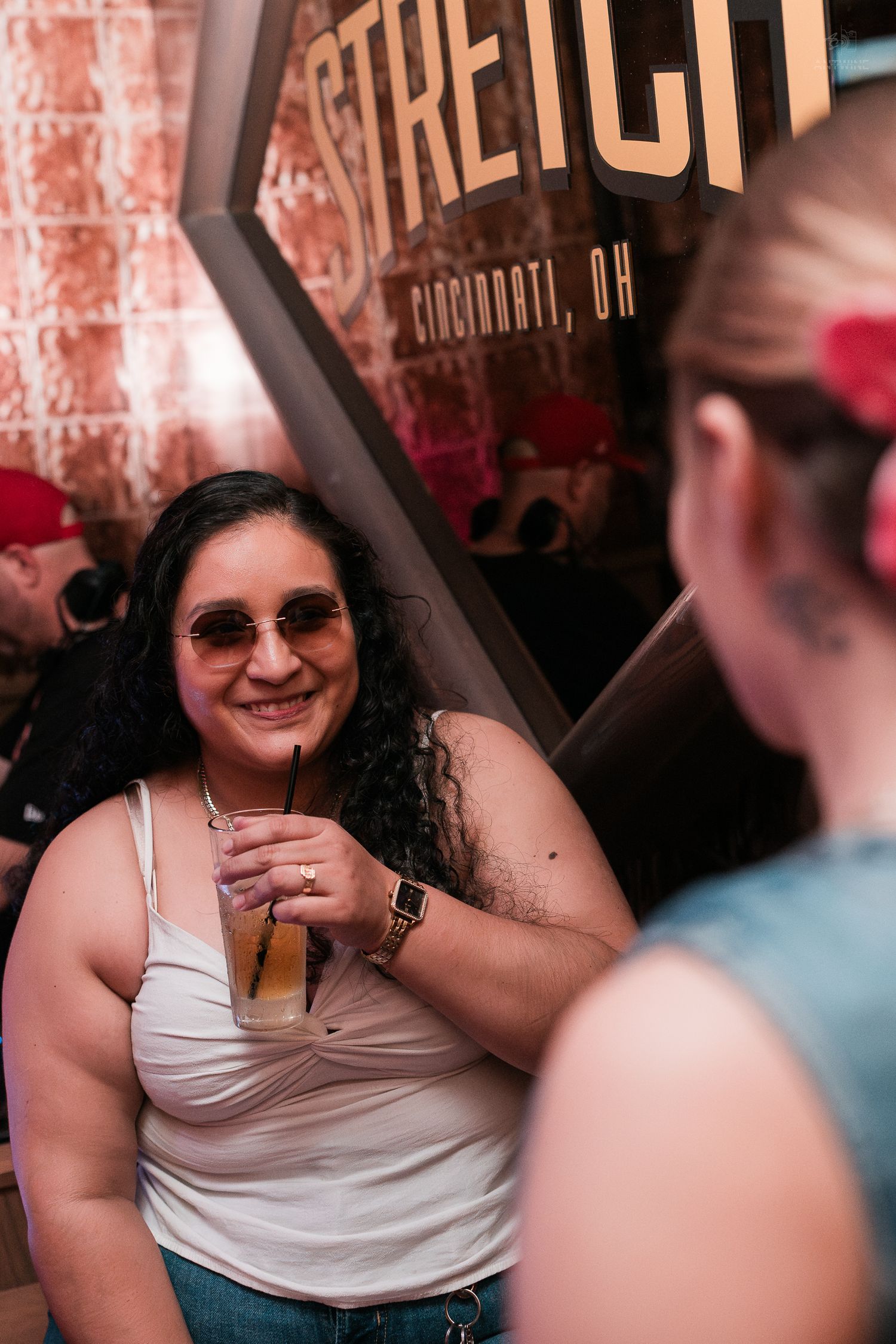 A smiling woman with curly hair enjoys a cocktail at Stretch bar in Cincinnati, OH.
