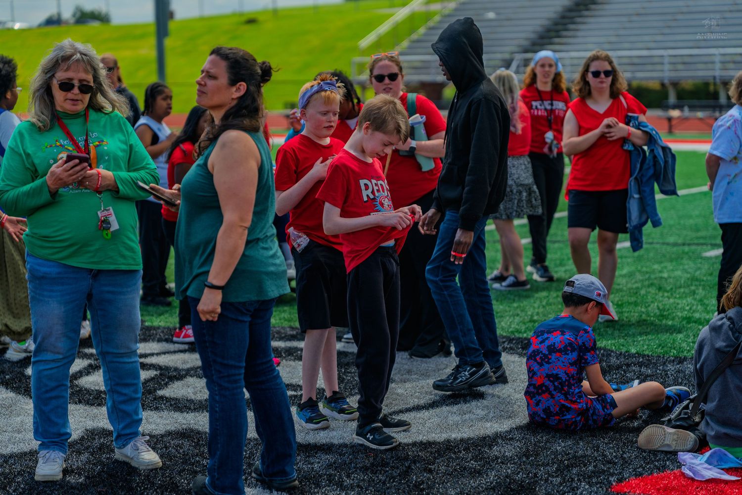 Students and teachers gather on a school athletic track field during an outdoor group activity event.