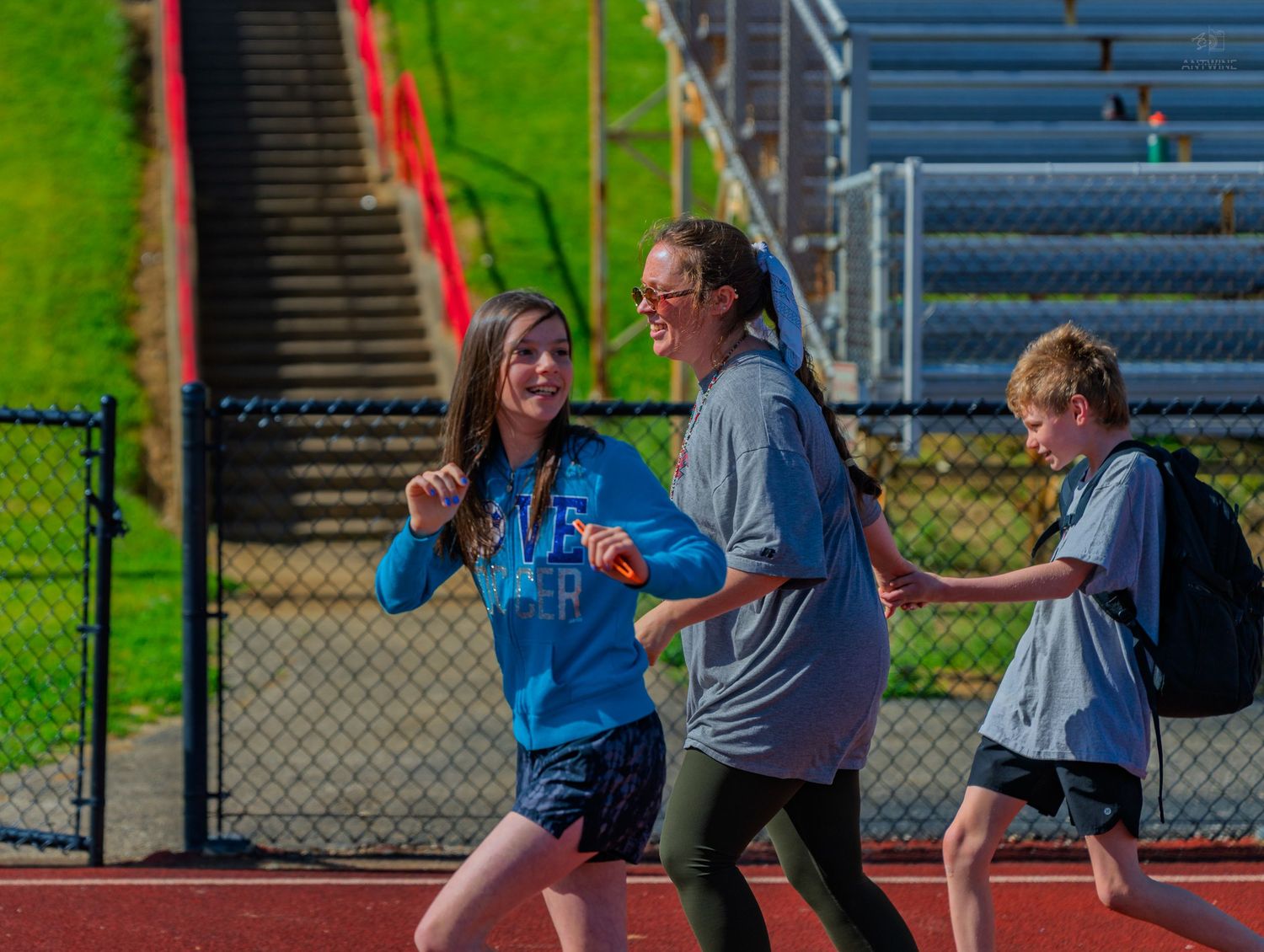 Three students jogging on a school track during outdoor physical education class on a sunny day.