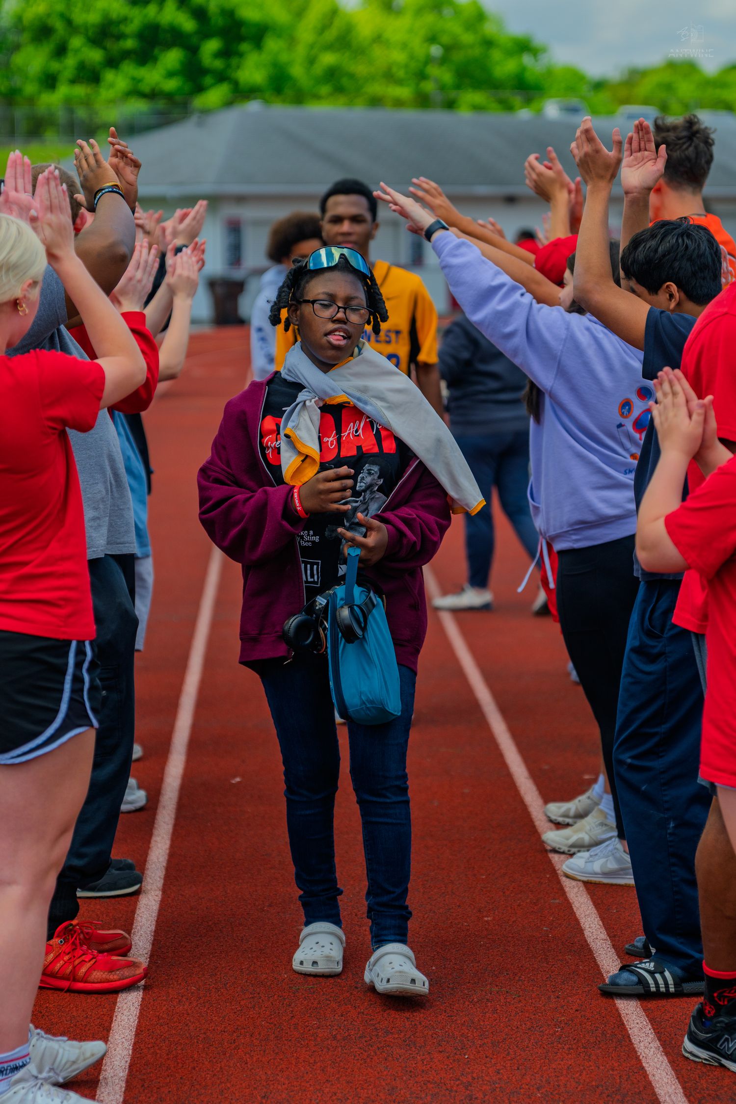 Young student walks through a high-five tunnel on a red running track during a school sports event.
