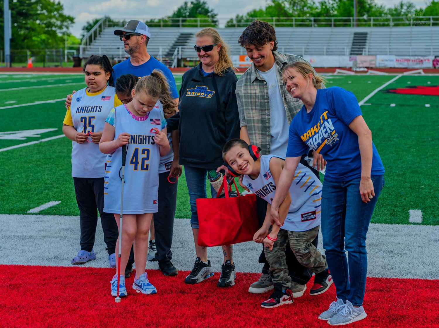 Group of kids and adults in Knights jerseys posing together on a red turf football field during a sports event.